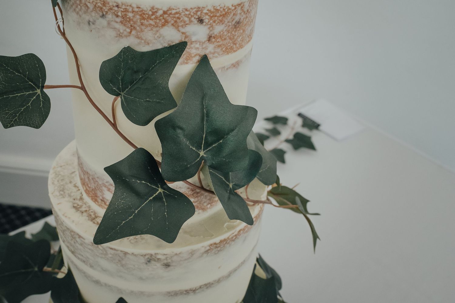 Elegant white wedding cake decorated with fresh green ivy leaves.