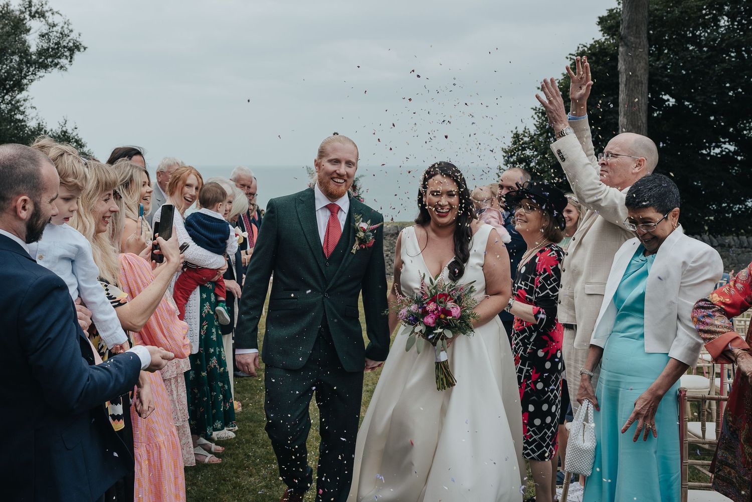 Wedding couple walking through shower of confetti with guests lined up on sides.