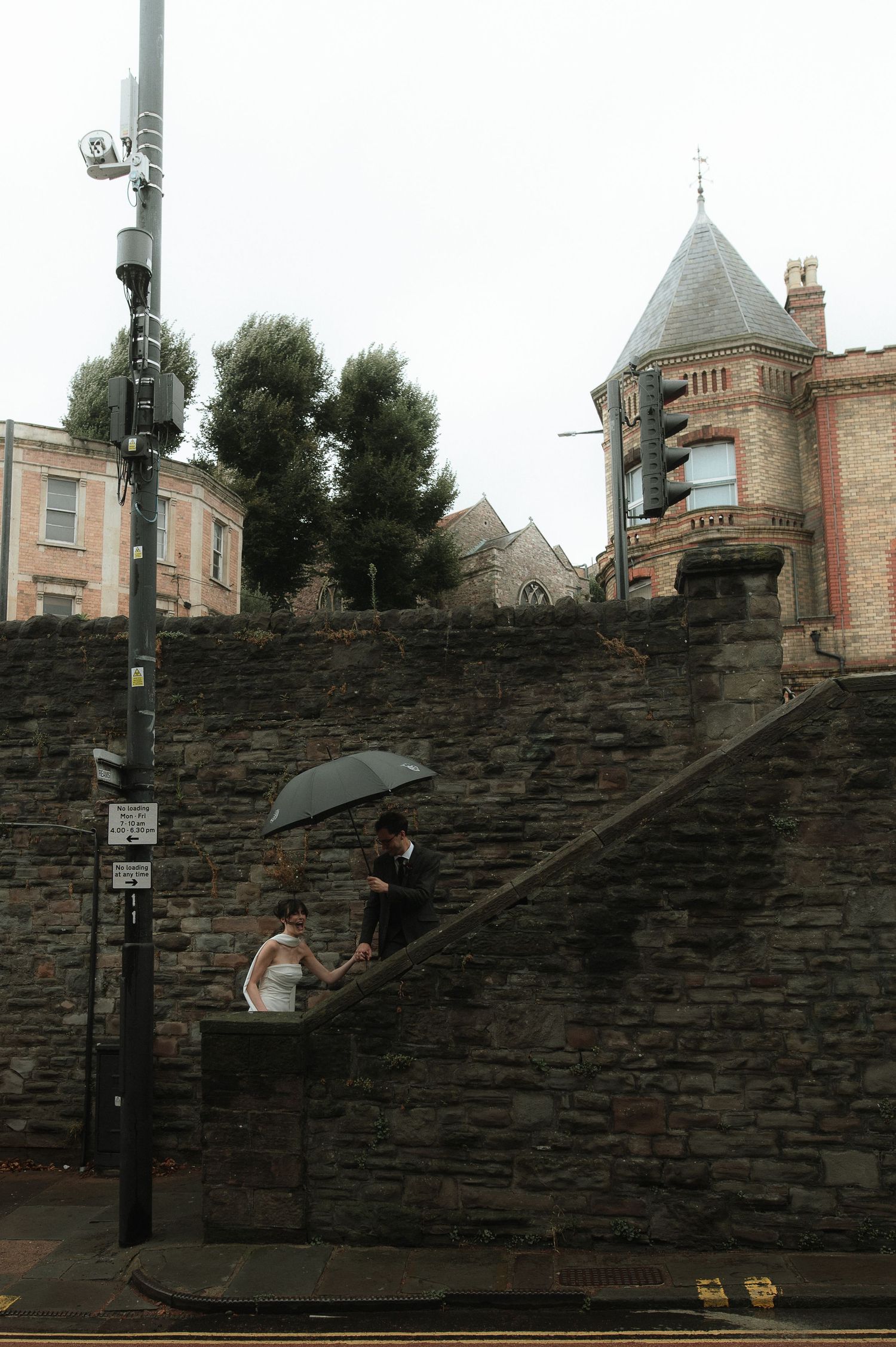 A person with an umbrella walks along a curved stone wall in Edinburgh during an overcast day.