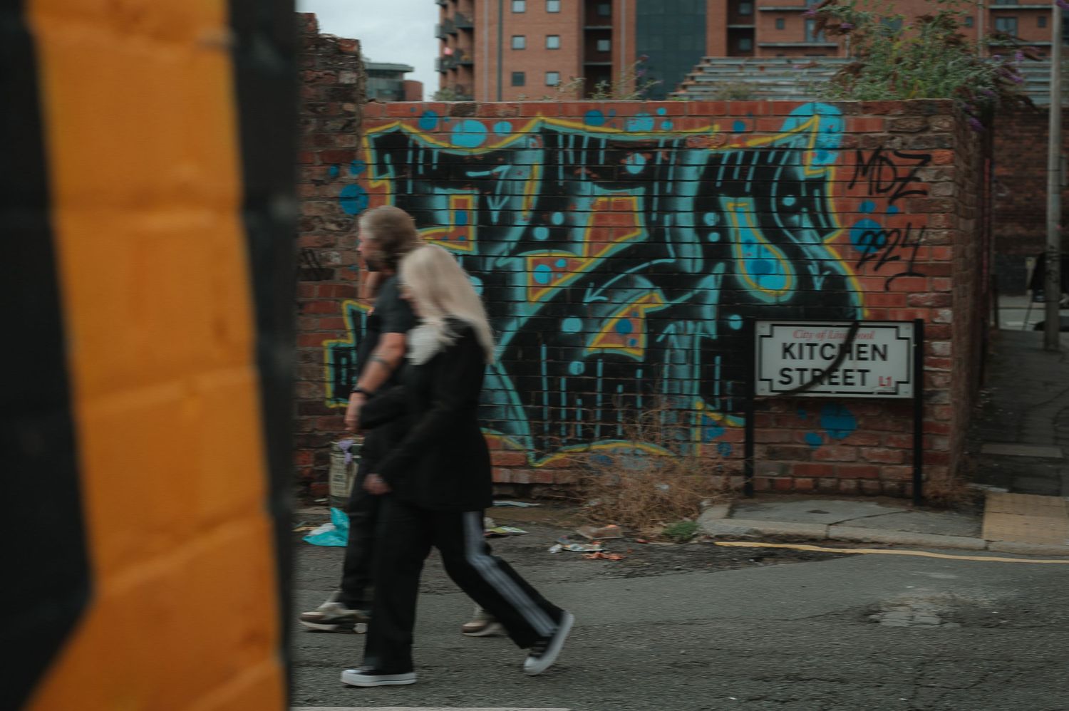 Person walking past vibrant turquoise graffiti art on brick wall in urban setting with motion blur effect.