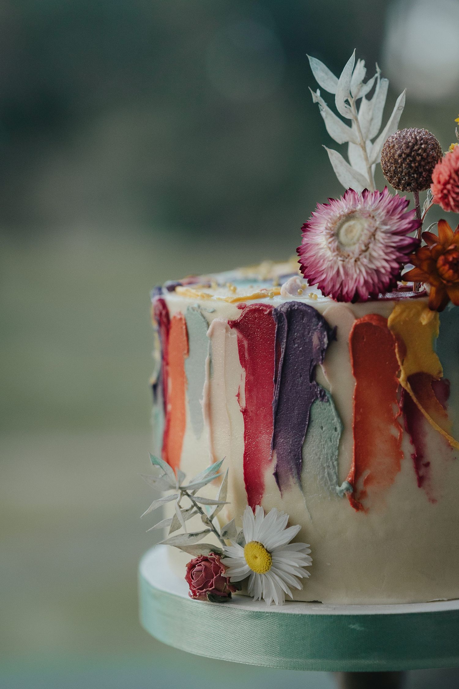 Artistic wedding cake decorated with colorful drip design and fresh flowers.