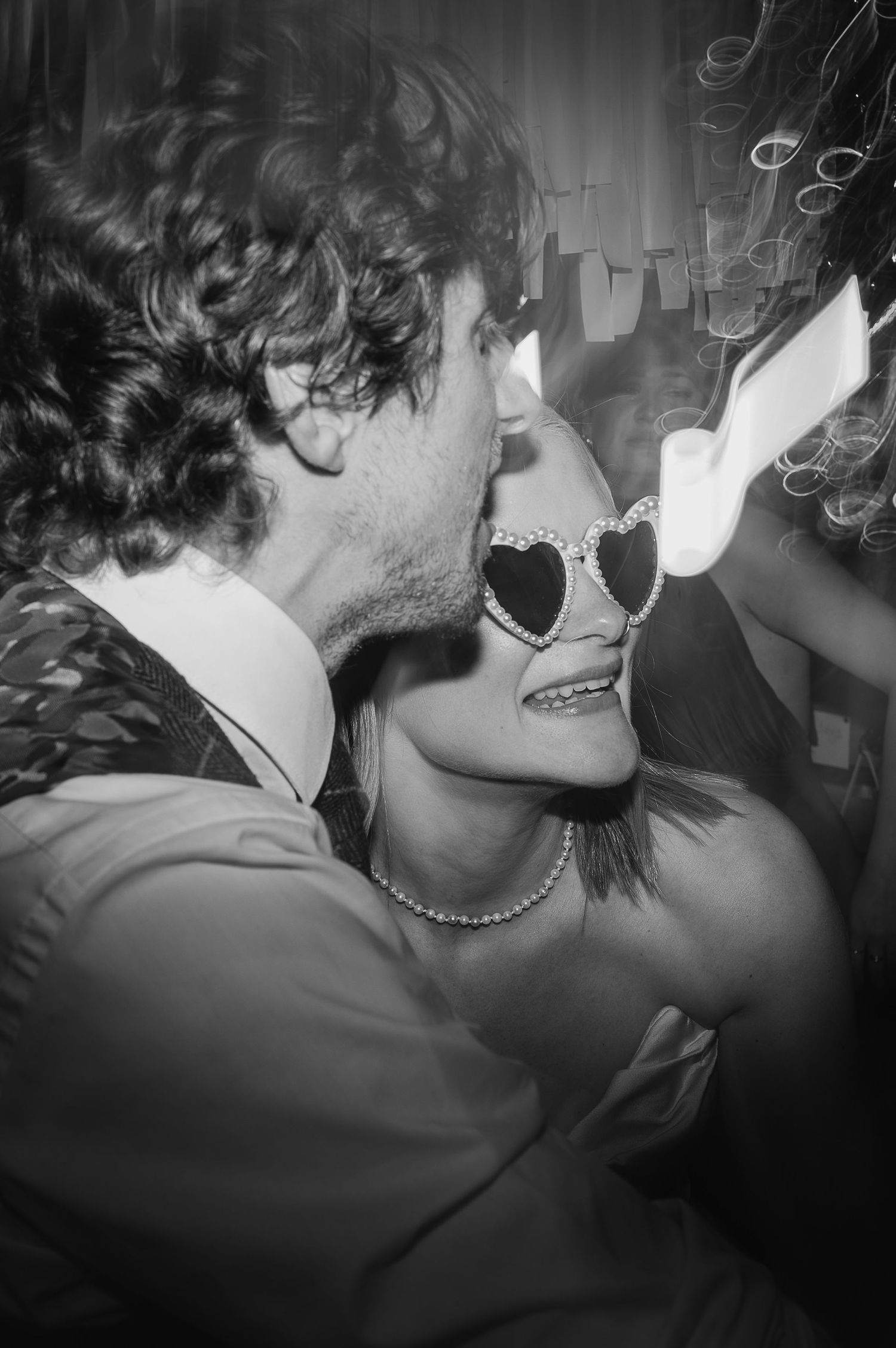 A stylish party-goer in heart-shaped sunglasses and formal attire enjoying a festive moment.