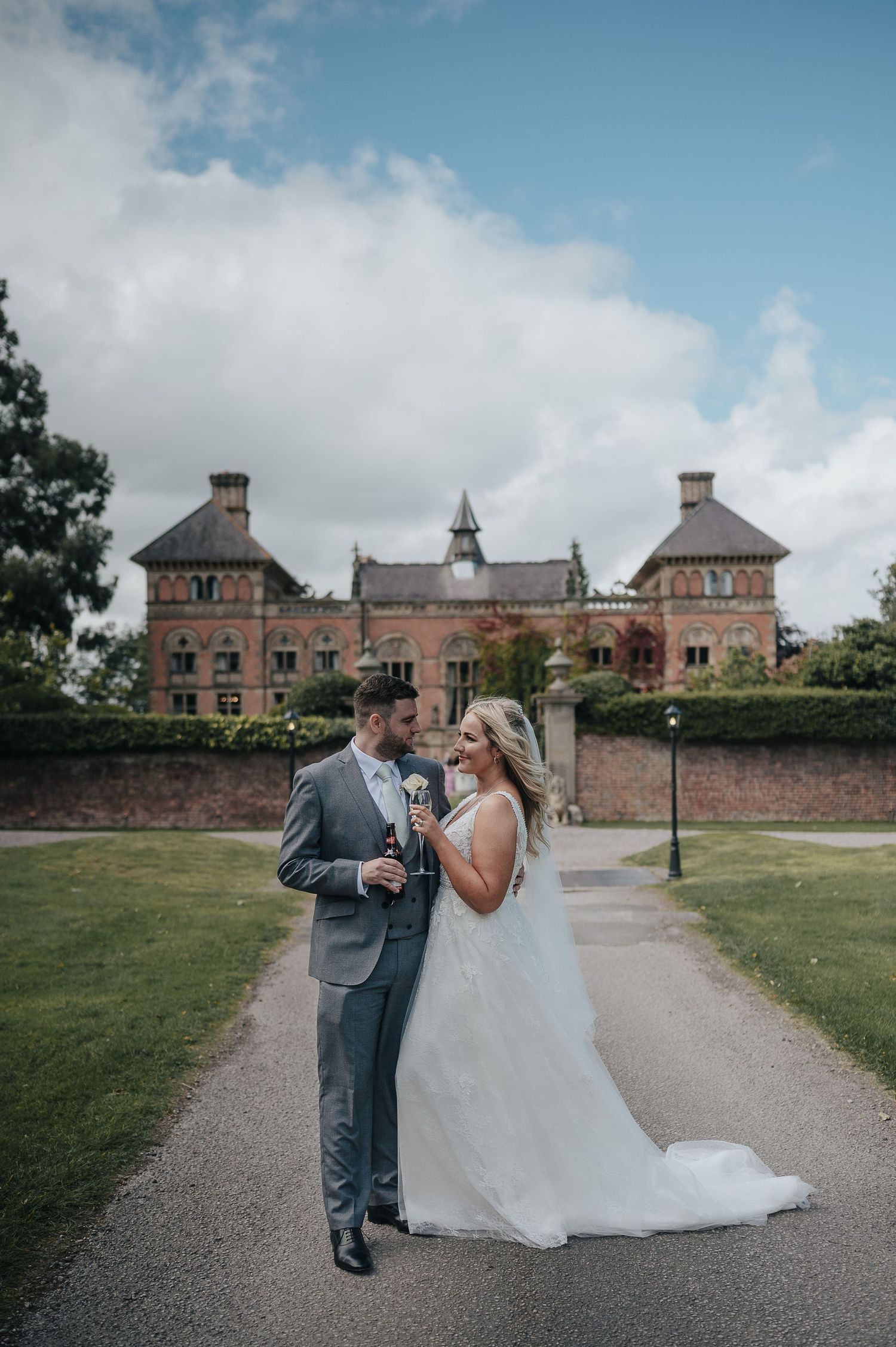Elegant wedding couple poses on path in front of historic brick manor house with manicured grounds.