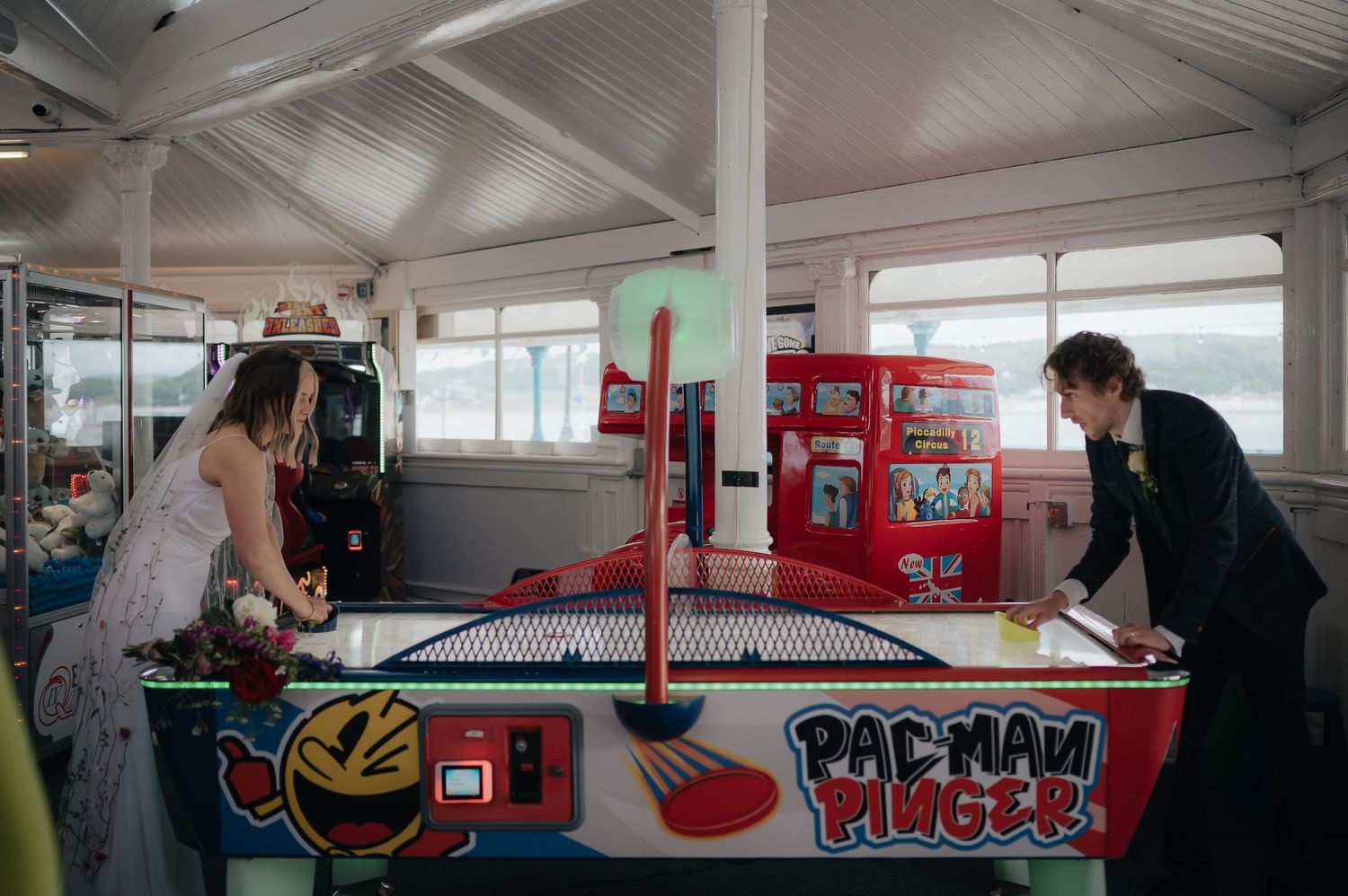 Couple in wedding attire playing air hockey at an arcade.