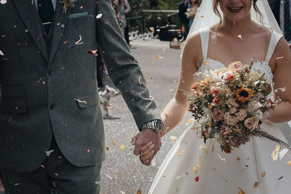 Close-up of couple holding hands with bridal bouquet and confetti in the air.