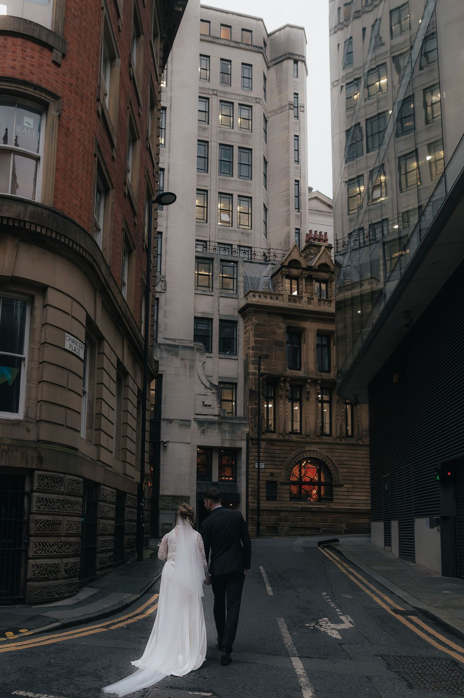A bride and groom walk down a moody urban alley lined with historic stone buildings in a city center.