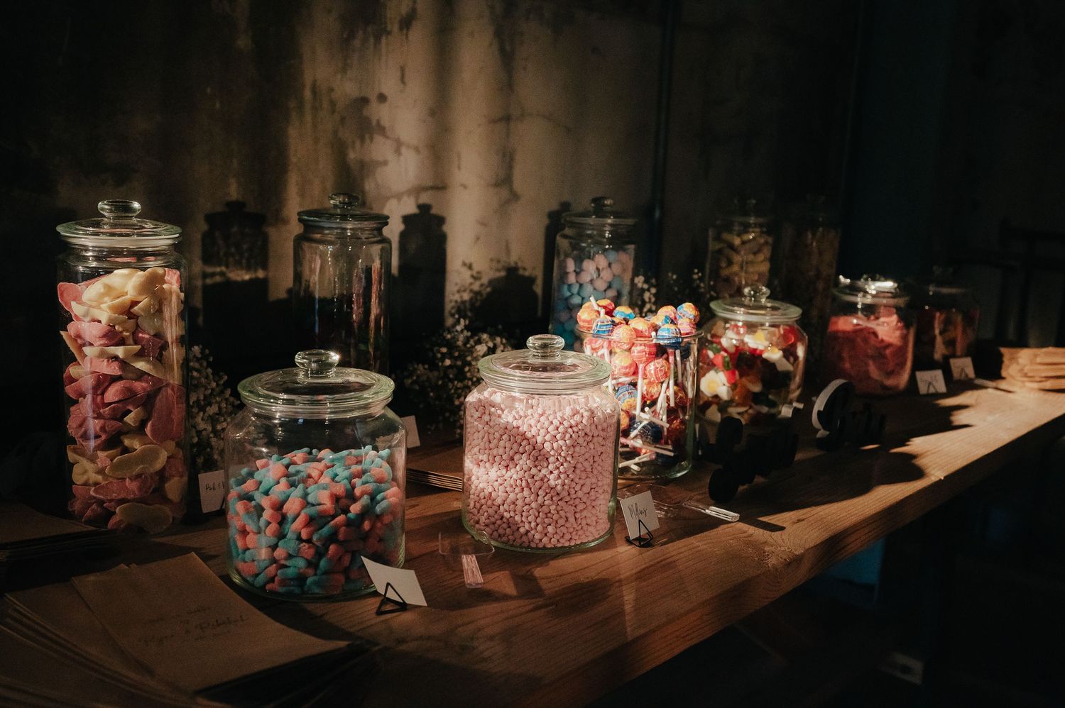 Glass jars filled with colorful candies arranged on a wooden table at a wedding reception.