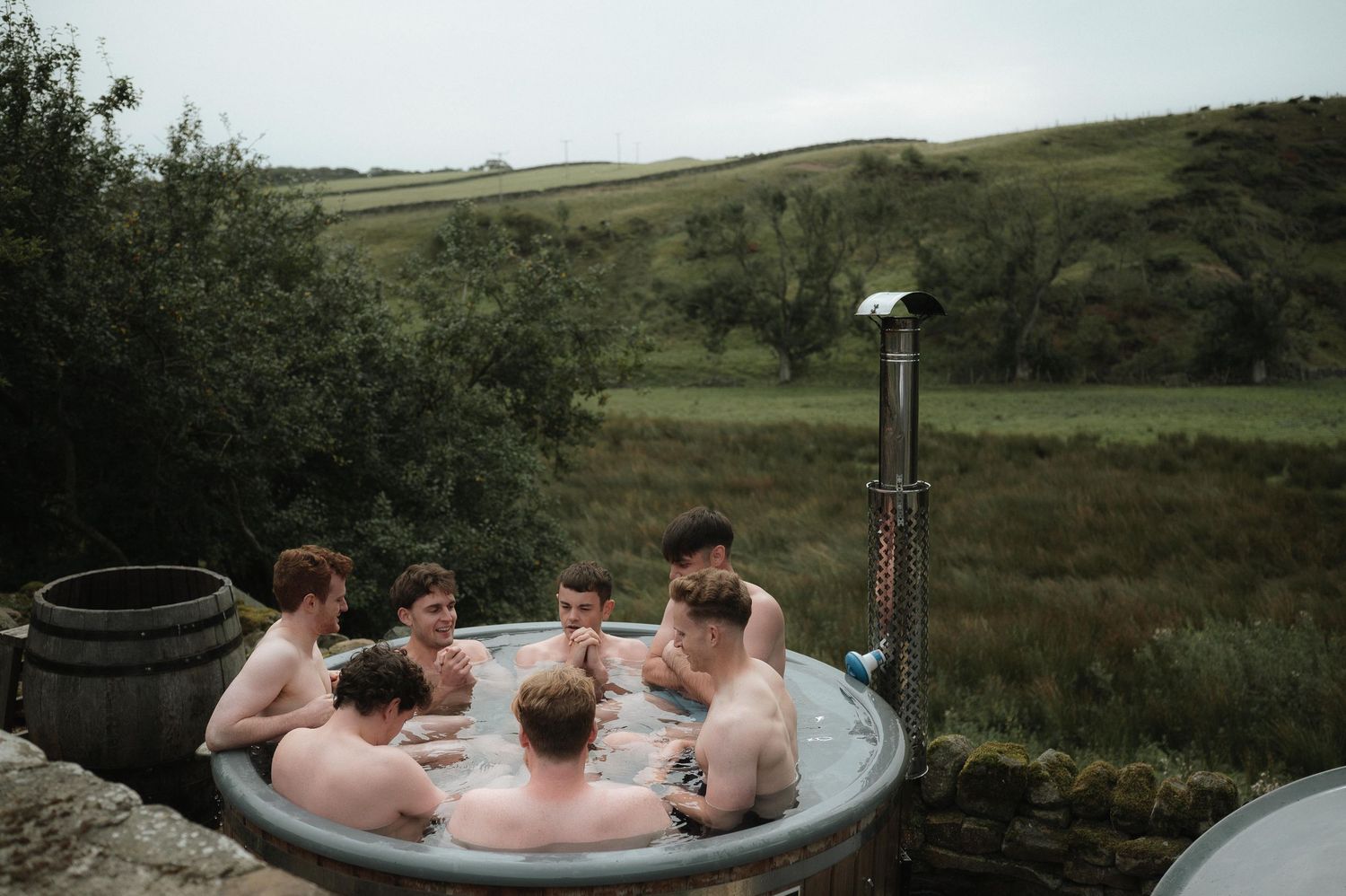 A group relaxes in an outdoor hot tub overlooking scenic rolling hills and countryside views.