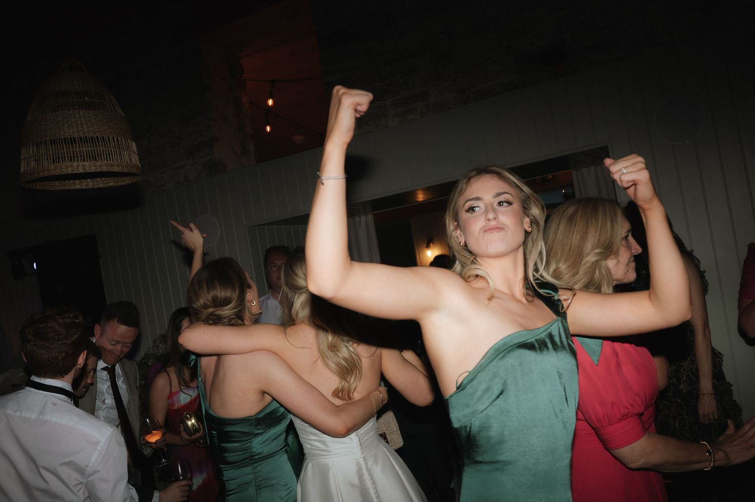 Wedding guests dancing and celebrating at dimly lit reception venue.