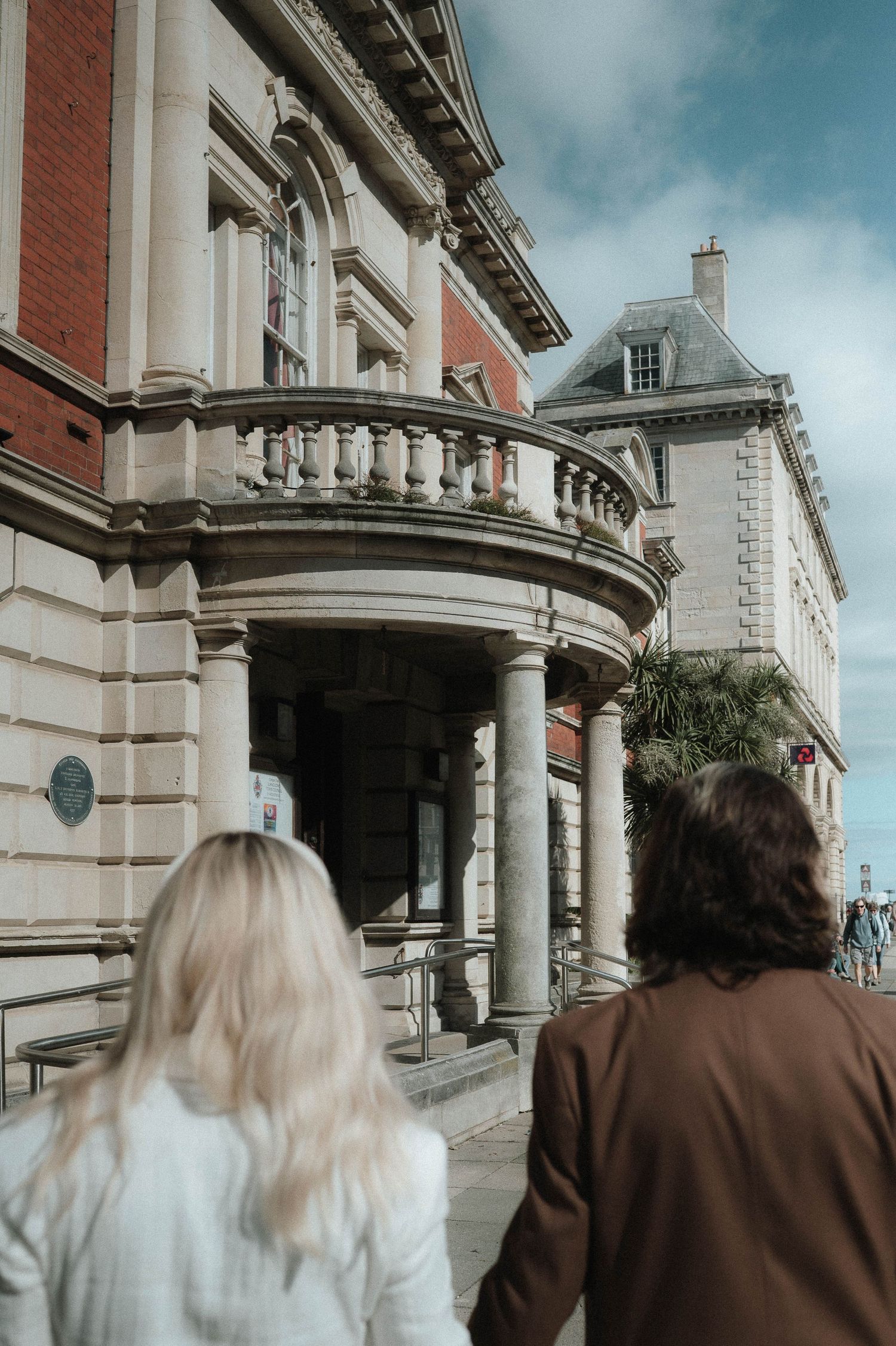 People walking outside a grand classical building with columns and ornate architecture.