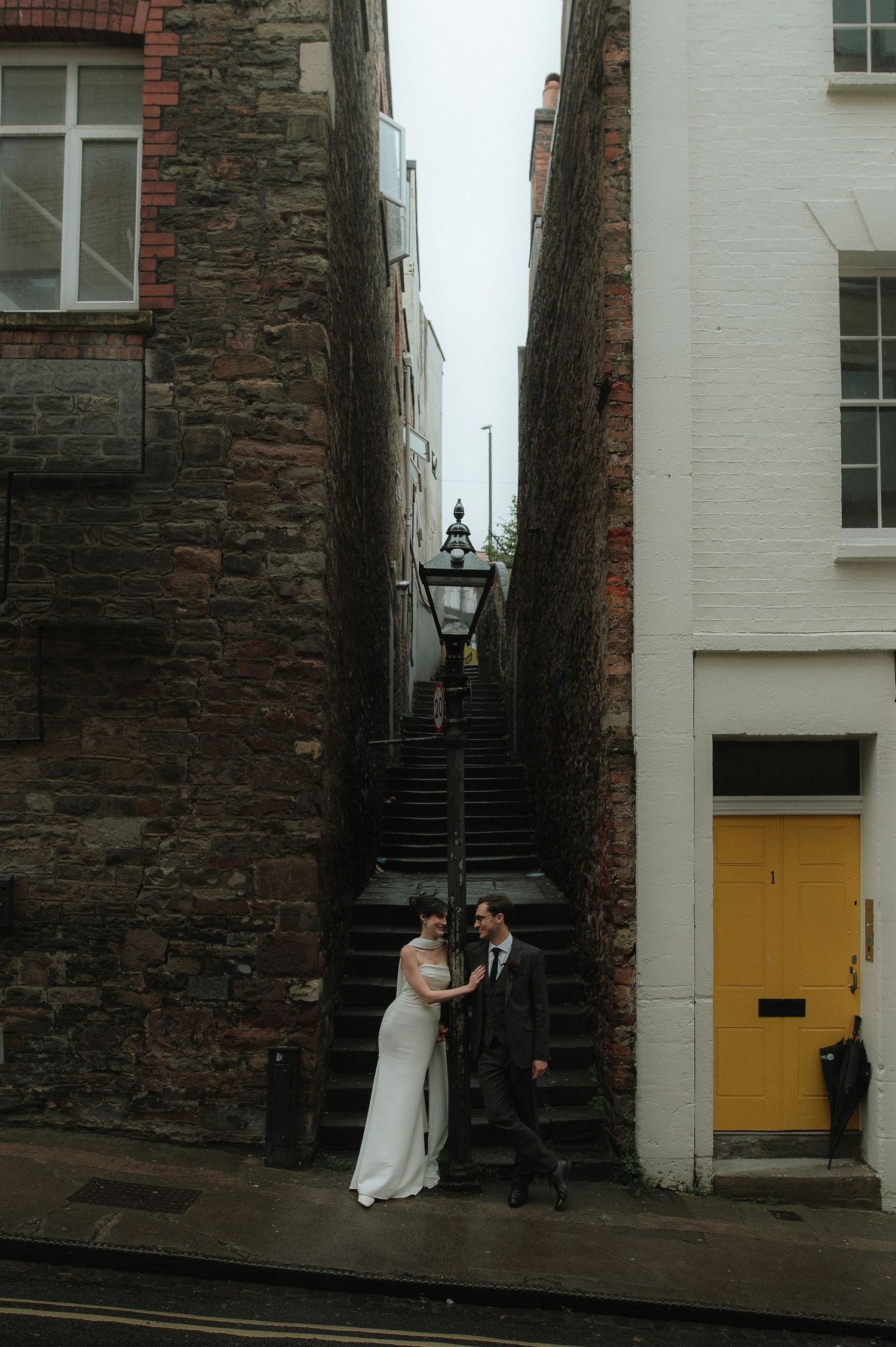 Wedding couple poses in charming alley with stone walls and yellow doors.