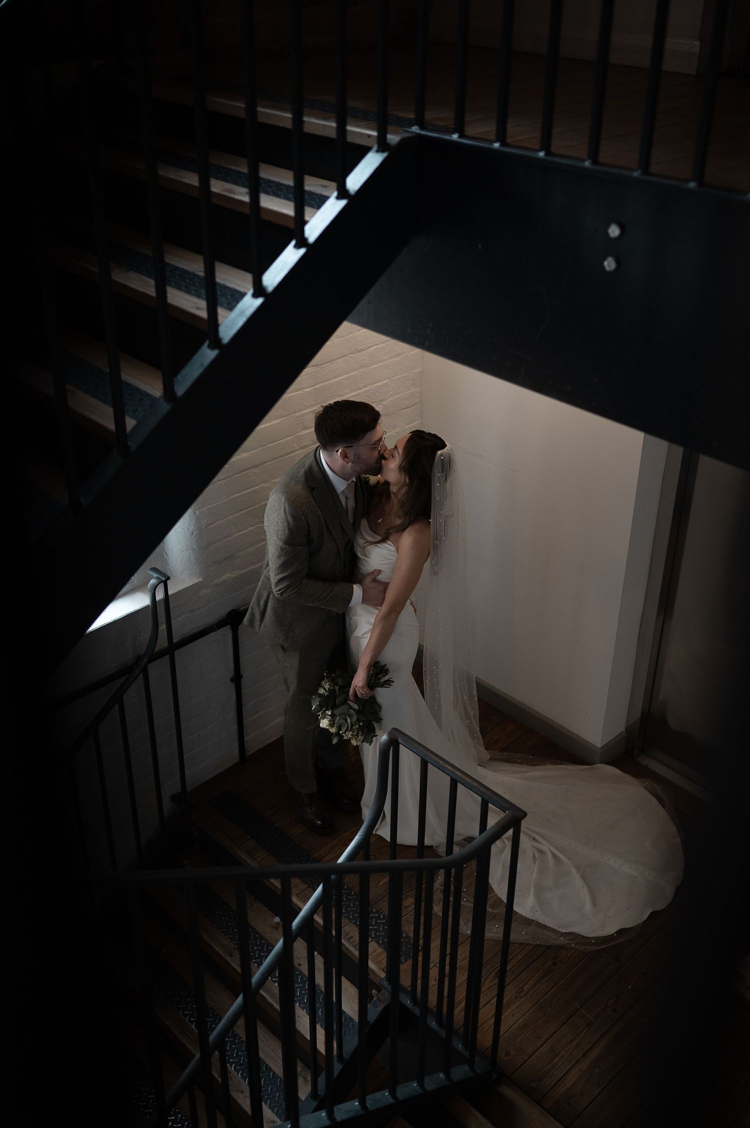 A couple descends a dramatic spiral staircase in formal wedding attire.