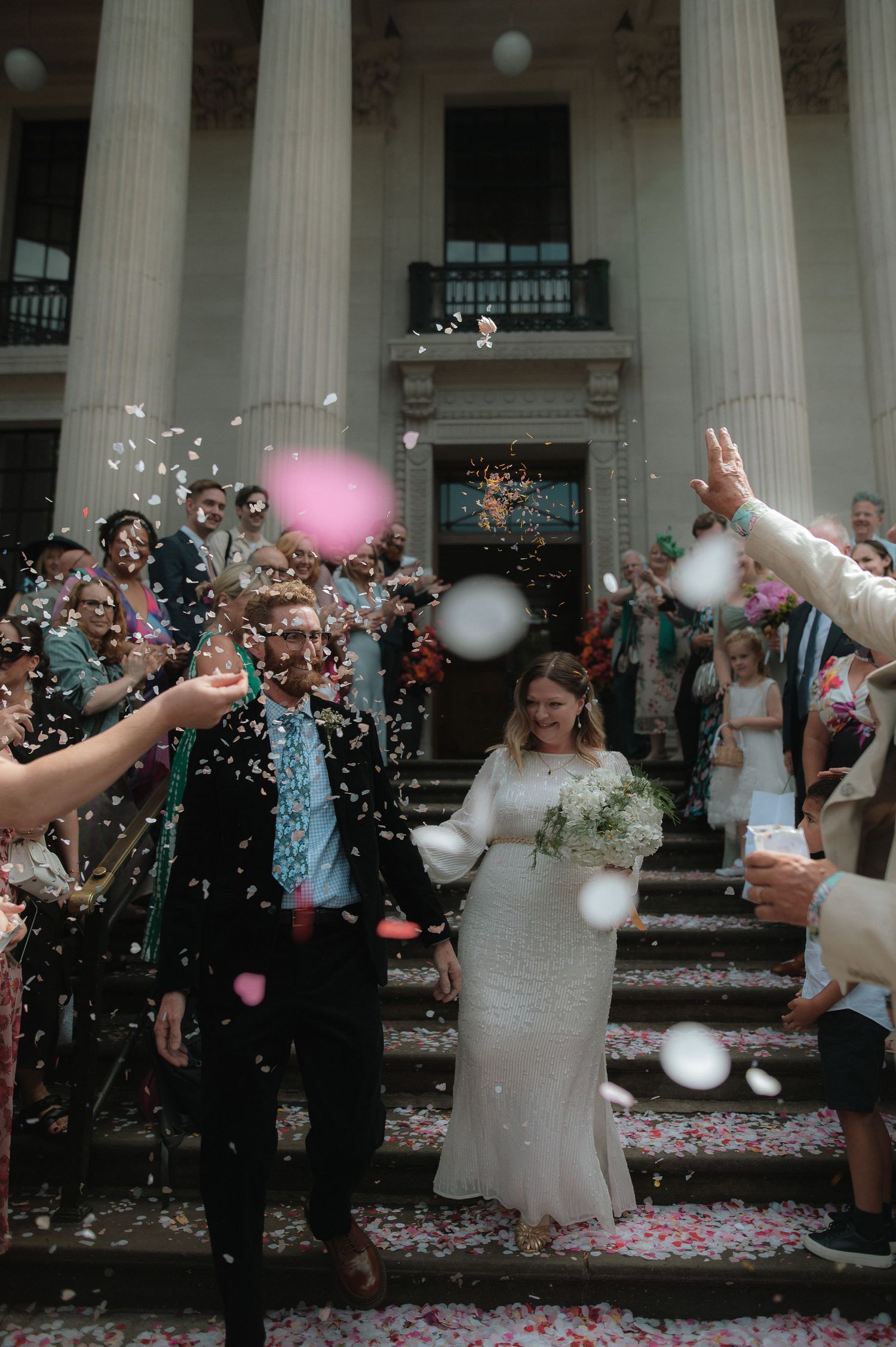 Wedding celebration with confetti and balloons in front of classical columns. London Wedding Photographer. London Wedding Photographer.
