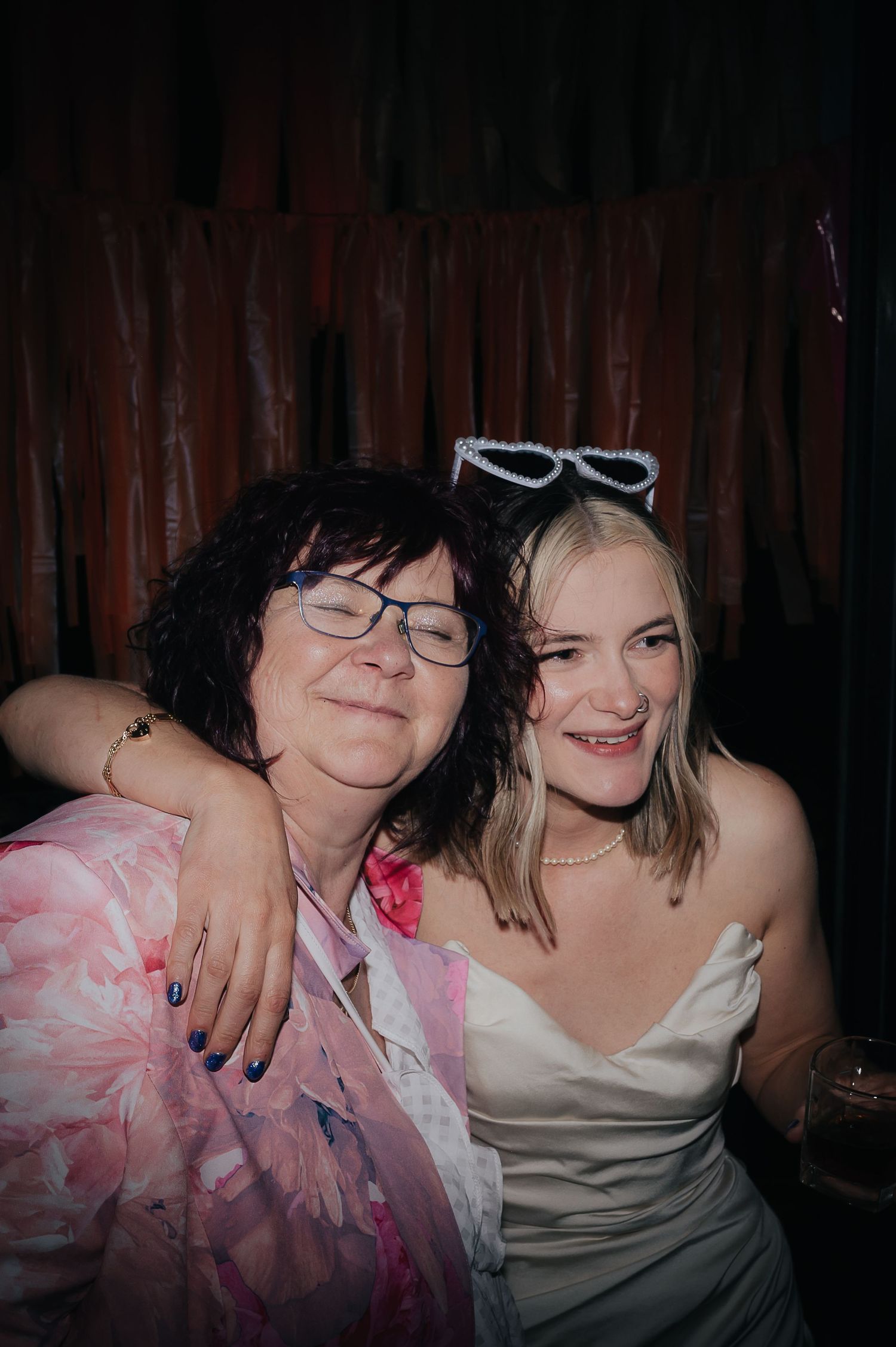 Two party guests share a warm embrace while posing for a casual photo at a celebration.