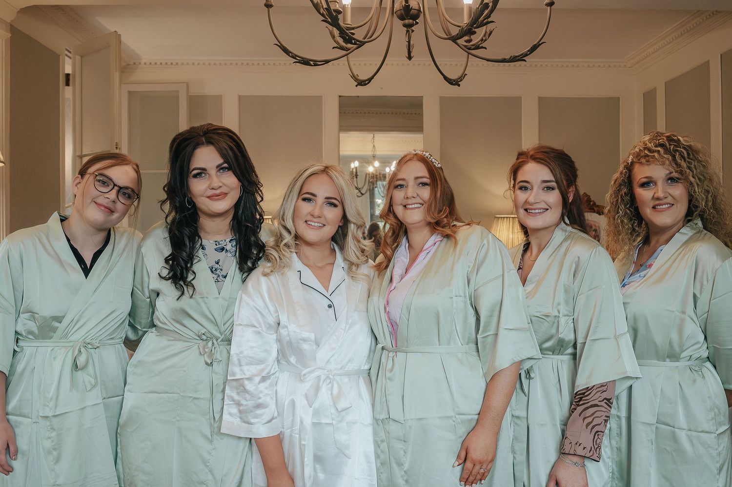 Group in matching mint green robes pose together in elegant room with chandelier.