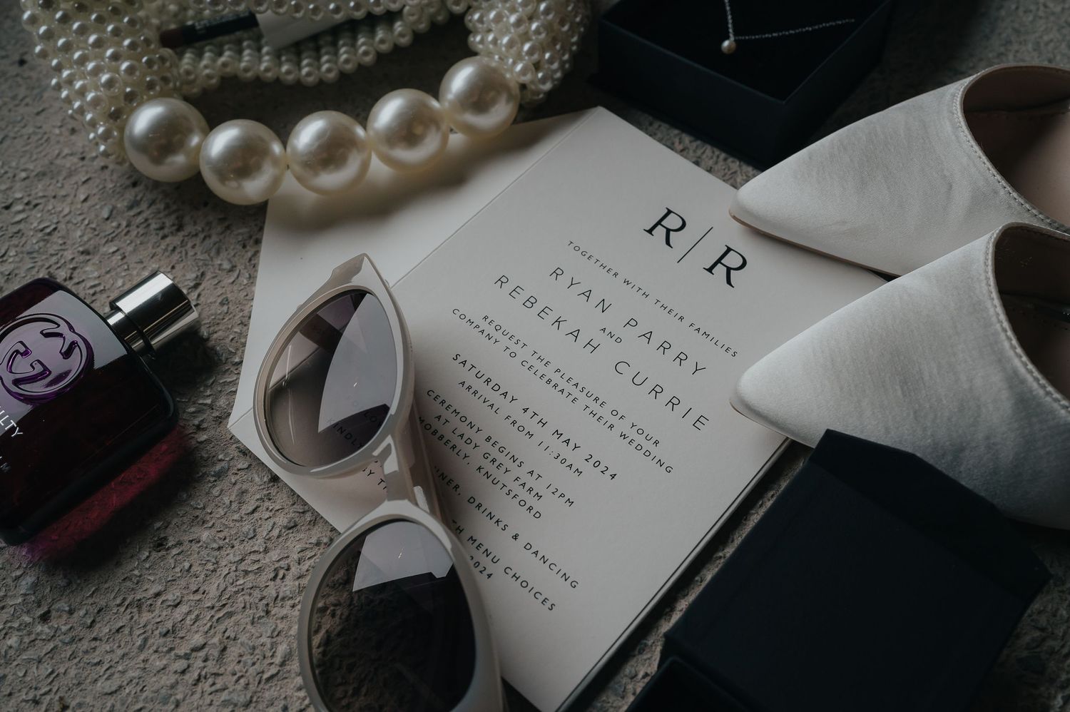 Wedding accessories including pearls, sunglasses, perfume and invitation on a light surface.