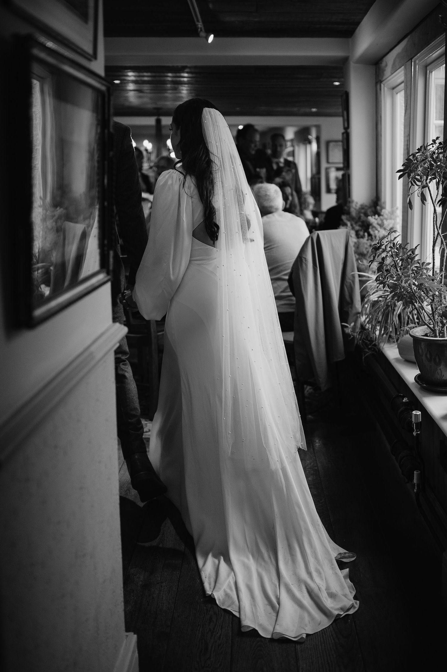 A bride in flowing white dress and veil stands in a hallway.