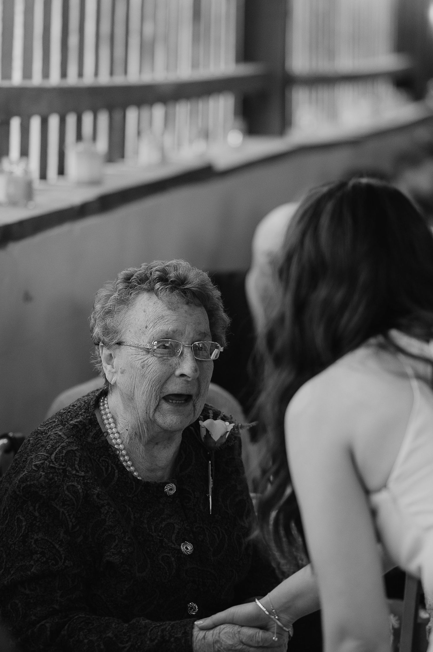 Black and white portrait of elderly woman in pearls sharing emotional moment at wedding.