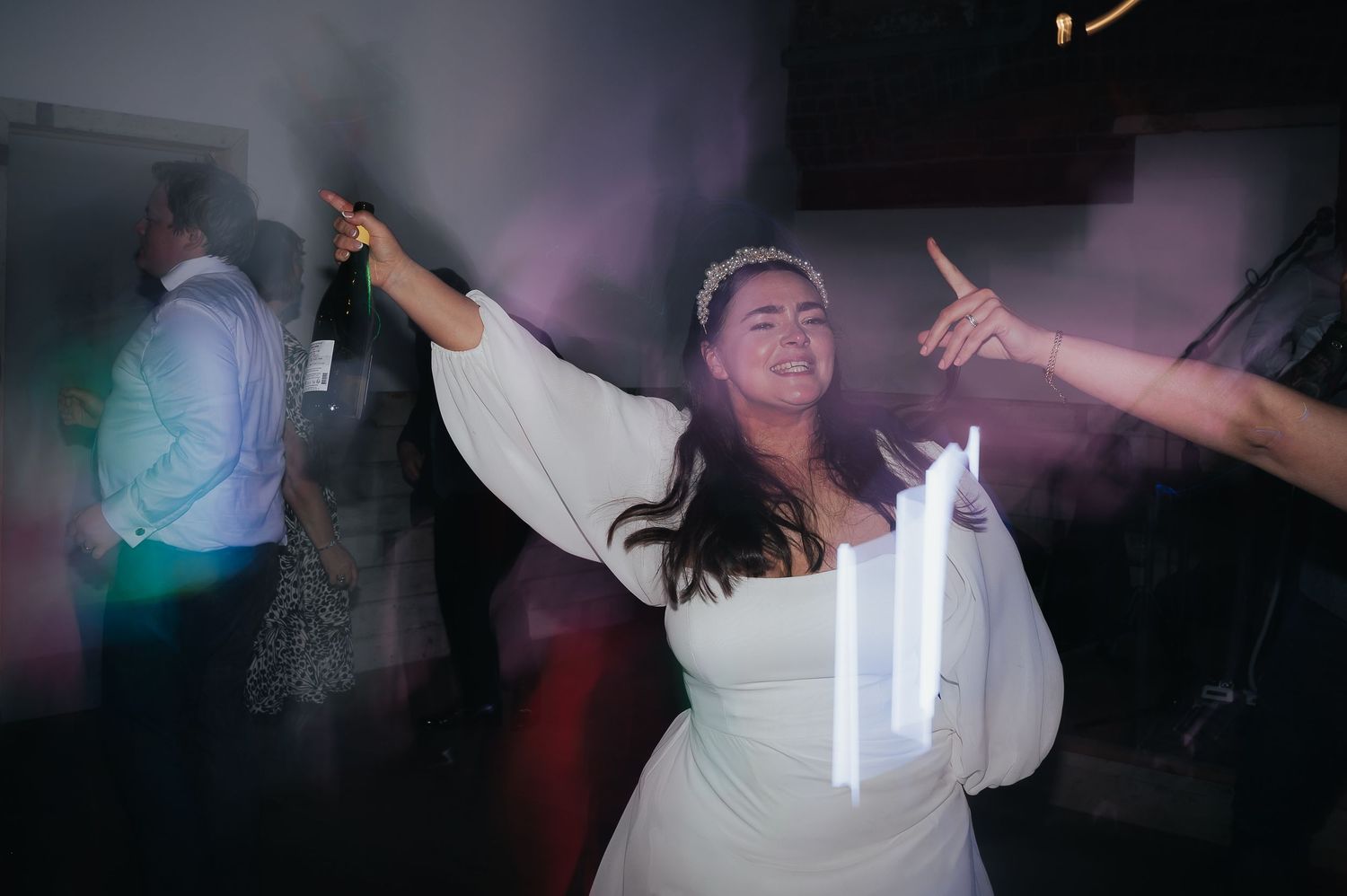 Person in white dress dancing joyfully at a party with raised arms and atmospheric lighting effects.