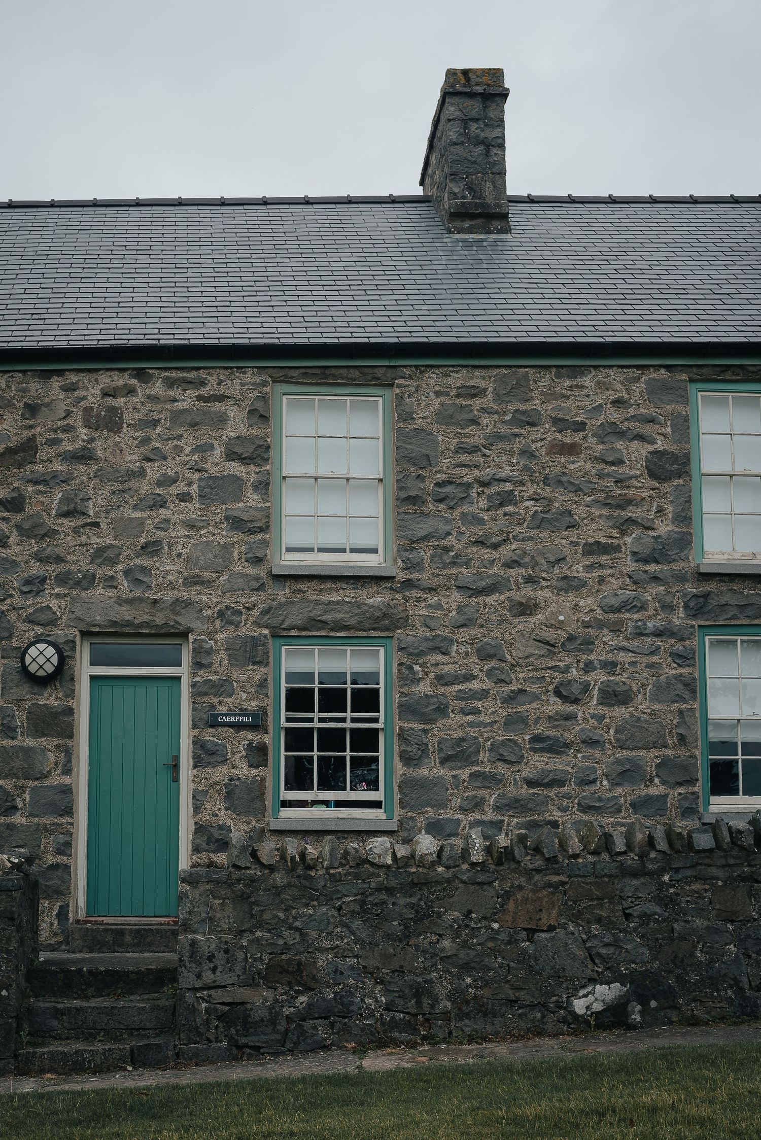 Traditional stone cottage with turquoise door and white windows in rustic setting.