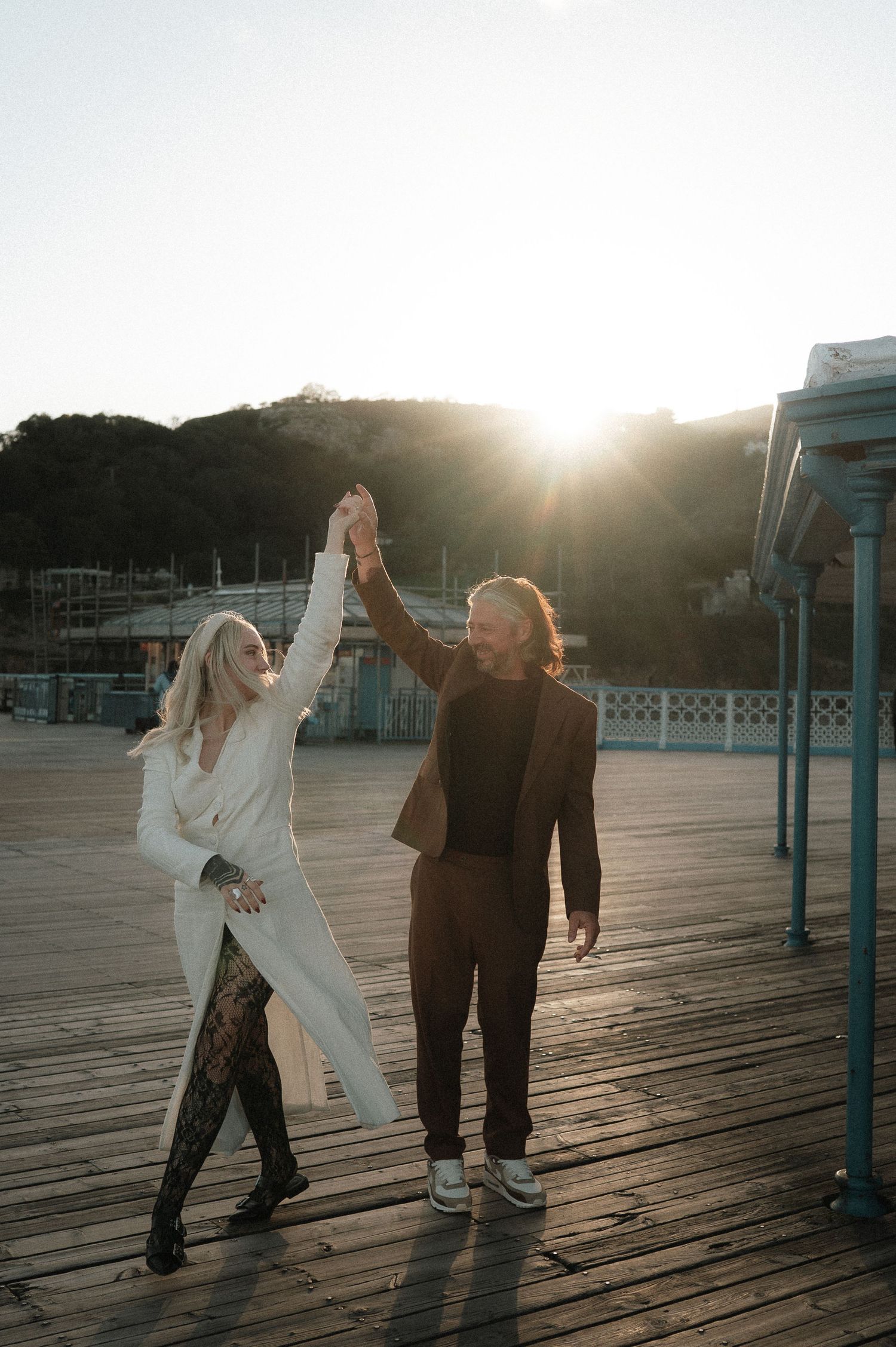 Couple dancing together on a wooden boardwalk at sunset, creating a romantic silhouette against the golden light.