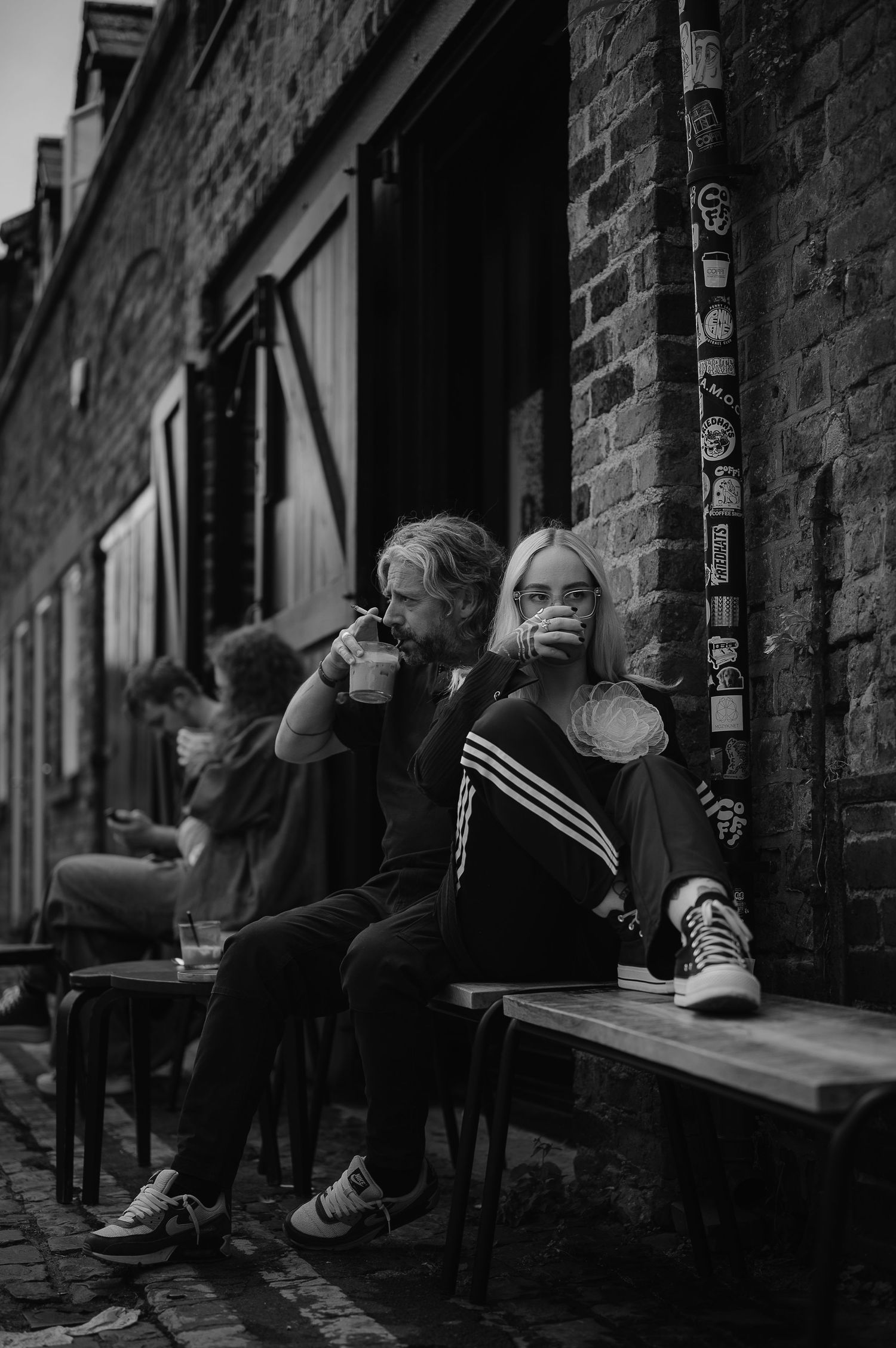 People sit and relax along a brick wall in an urban alley, creating a moody black and white street scene.