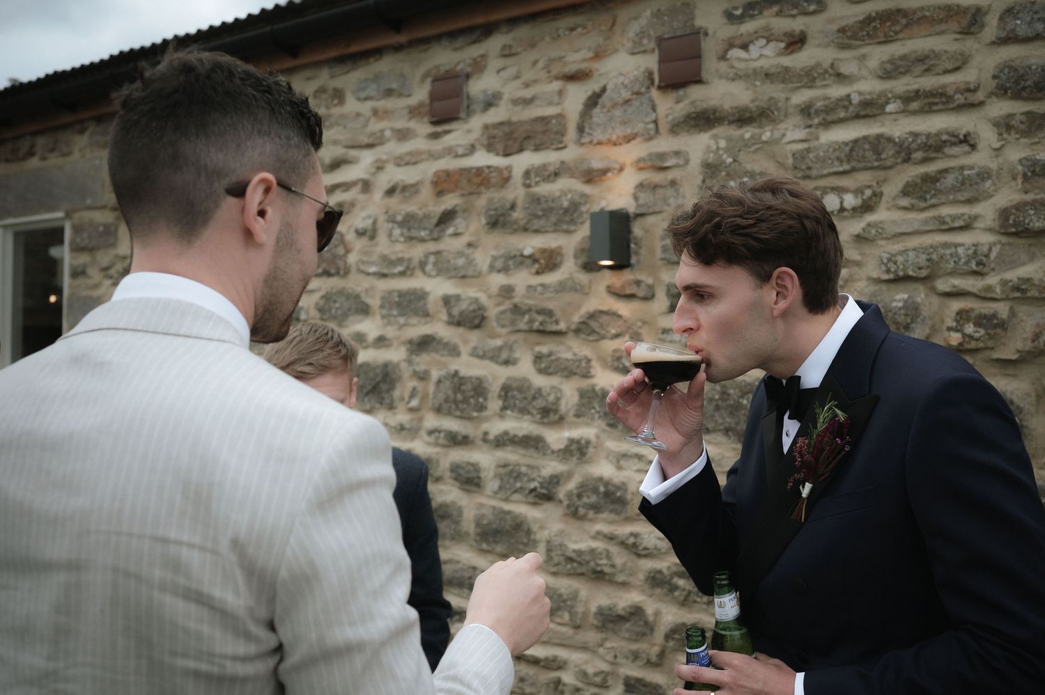 Groomsmen gathered outside a rustic stone wall during wedding celebrations.