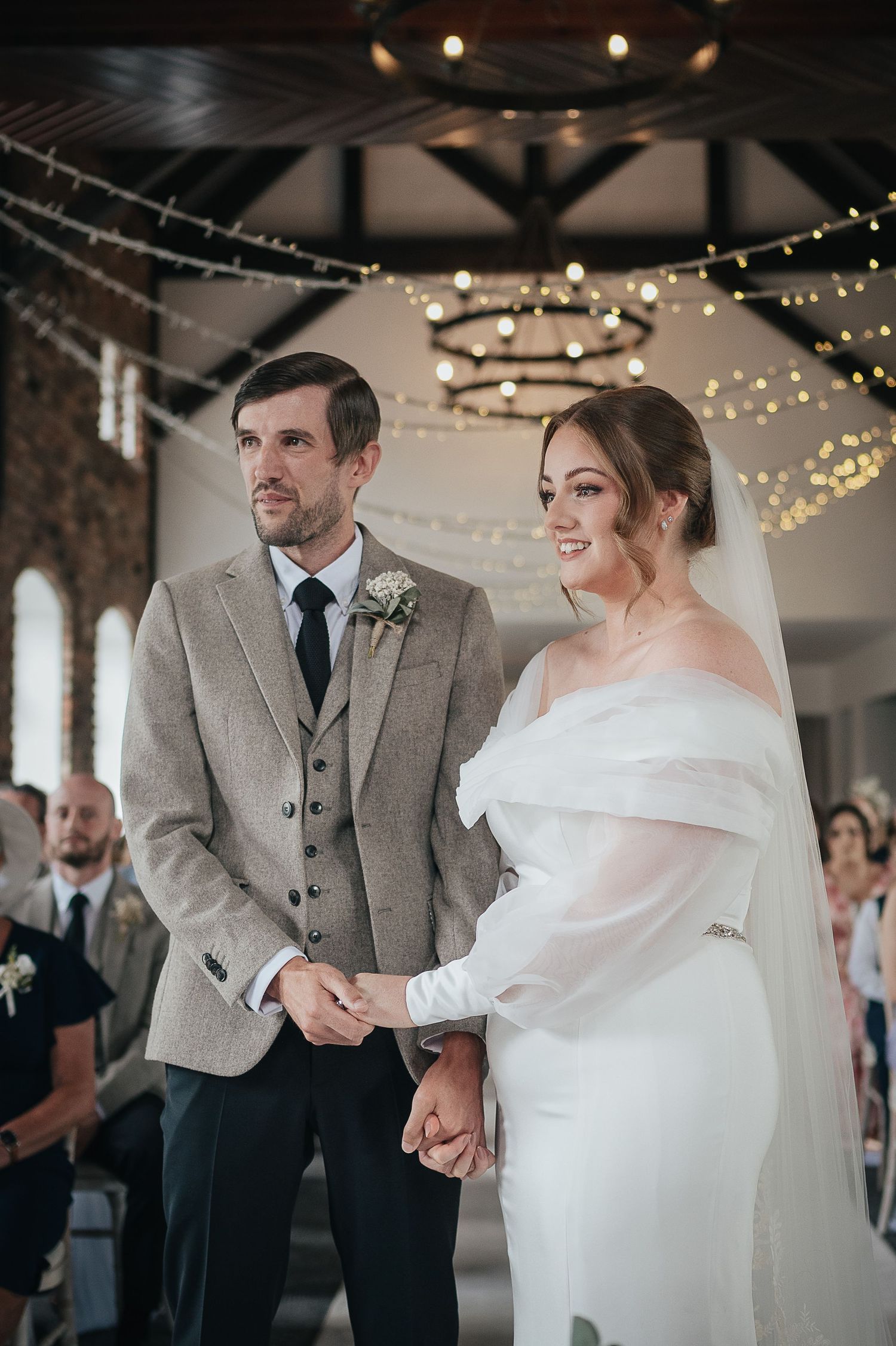 Wedding ceremony in rustic venue with exposed brick and twinkling fairy lights overhead.