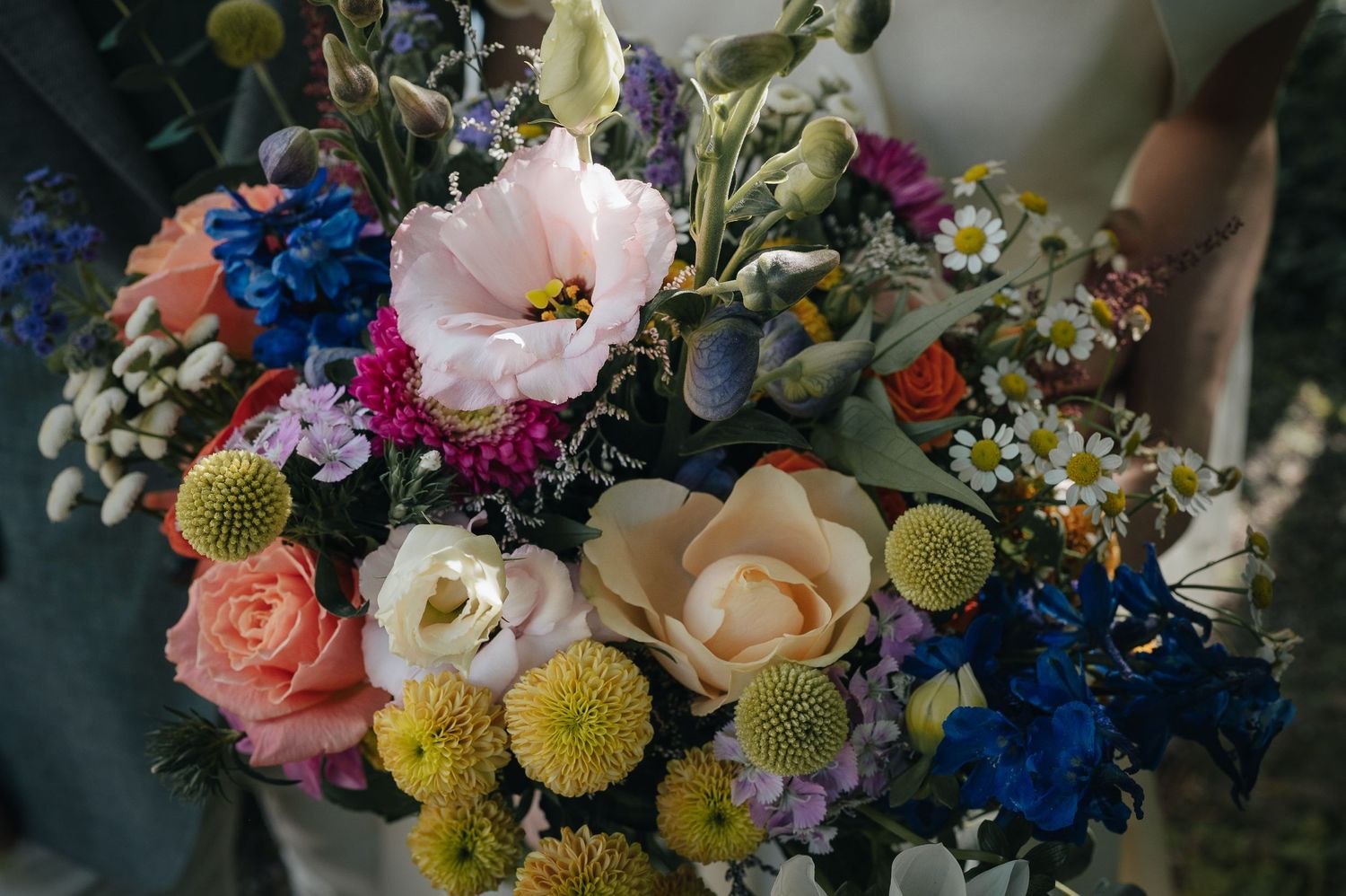 A vibrant wedding bouquet featuring pink, blue, and yellow flowers with mixed greenery.