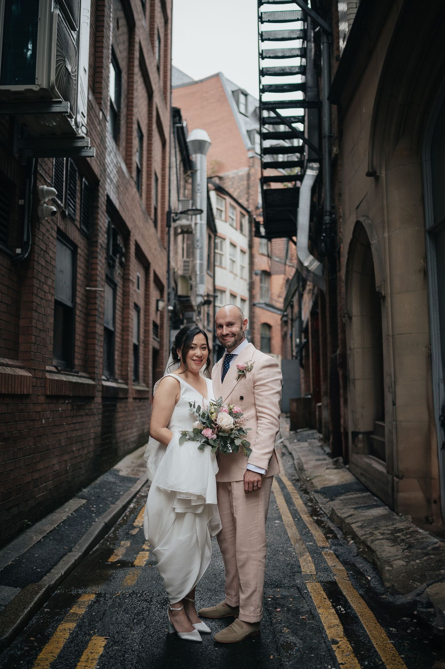 Wedding couple posing in an urban alley with brick buildings and yellow lines on the ground.