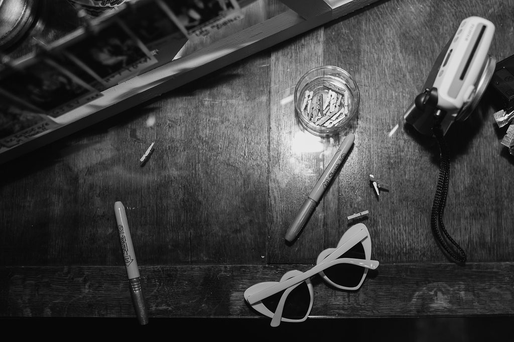 Black and white still life of sunglasses and wedding accessories on wooden surface.