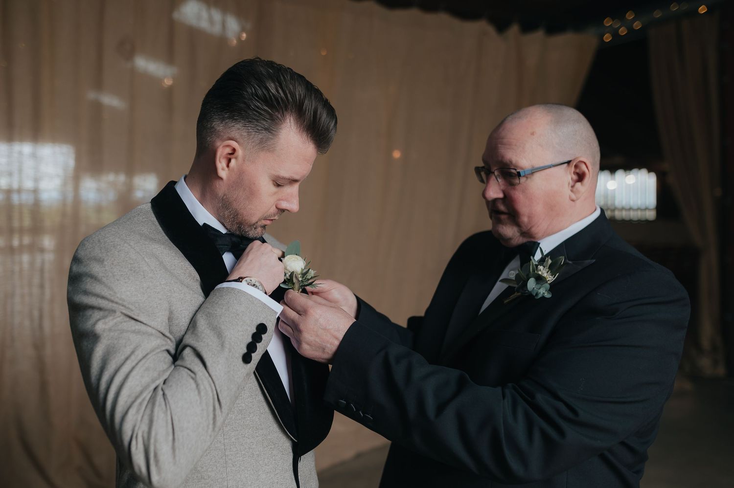A boutonniere being pinned onto a light gray tuxedo jacket during wedding preparations.