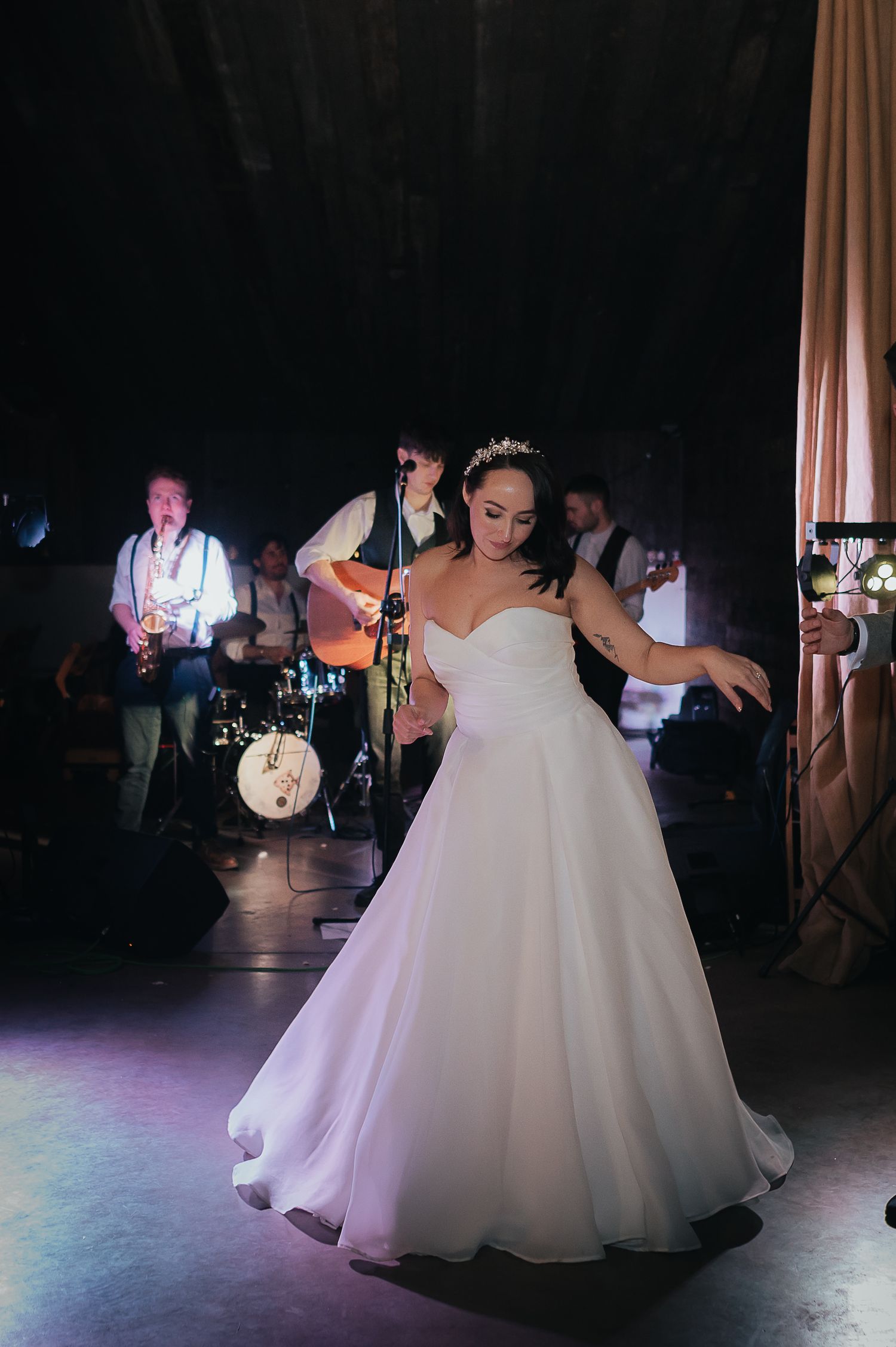 Bride in flowing white gown dances while live band performs on stage.