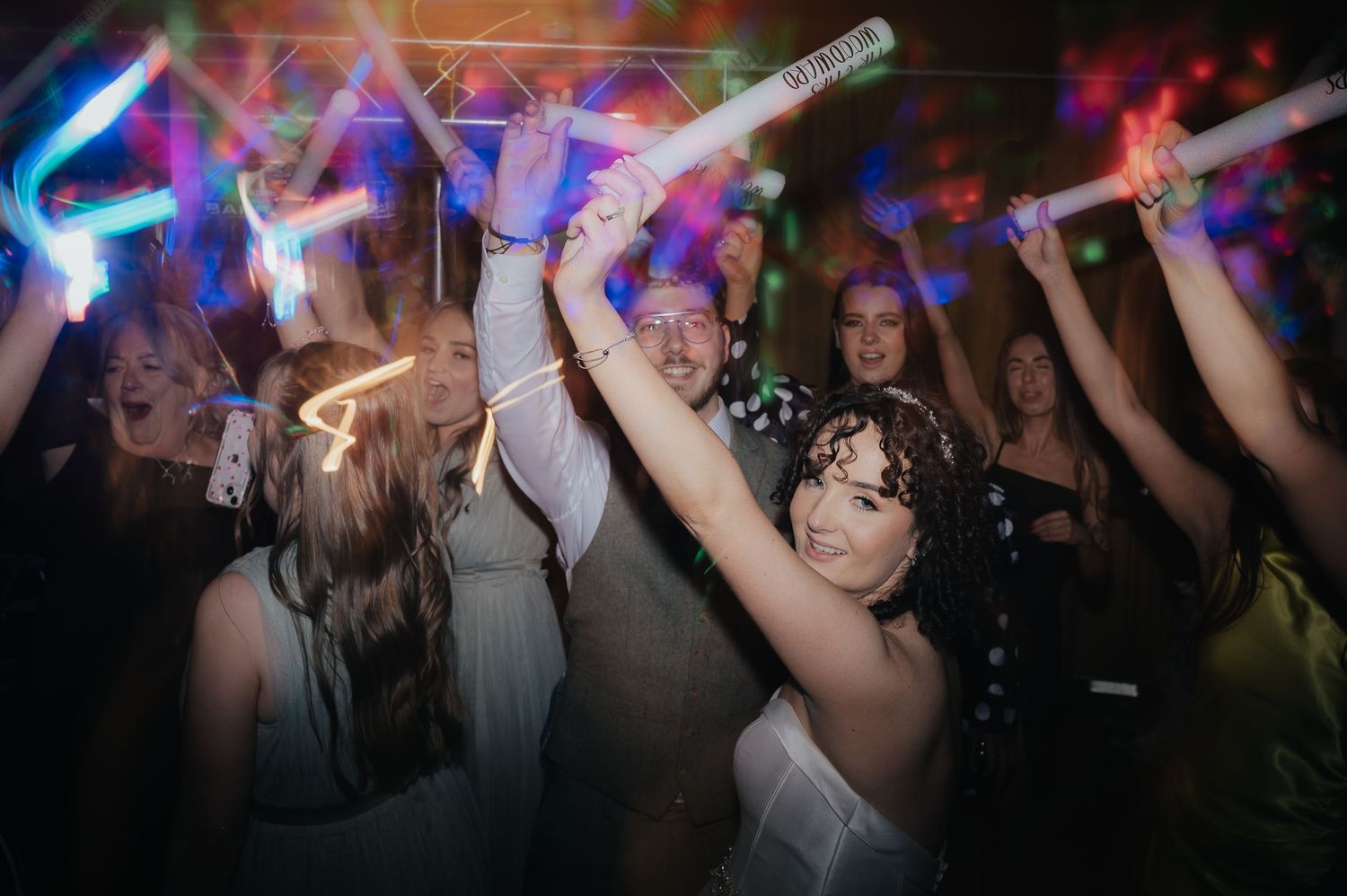 Wedding guests dancing and waving light-up sticks on a vibrant dance floor.