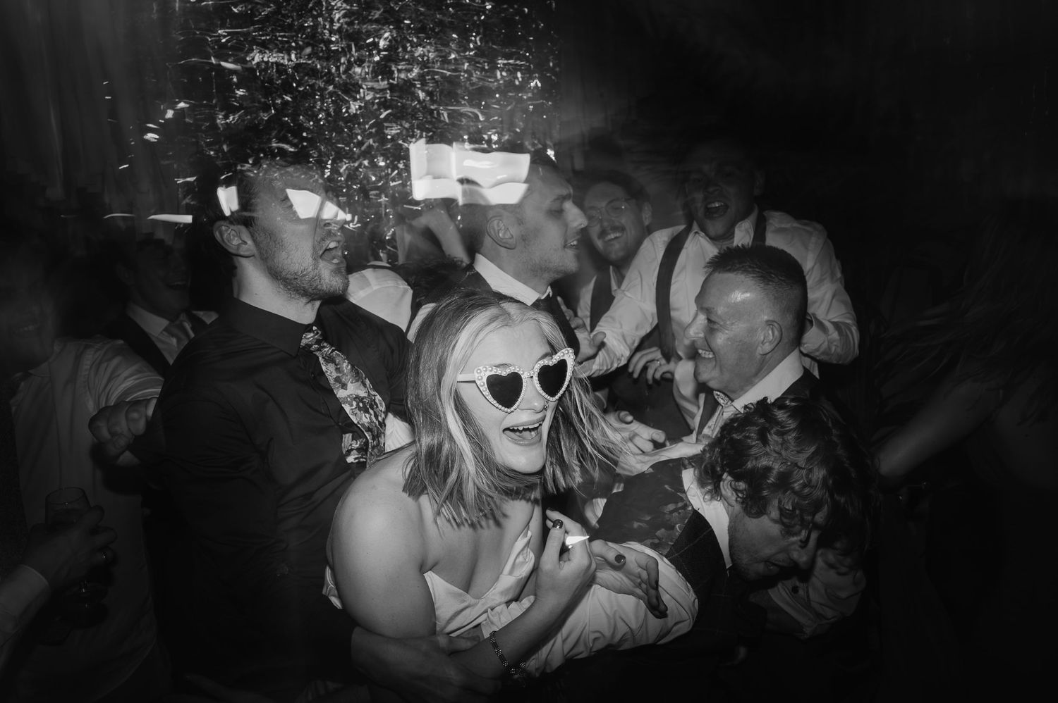 Black and white photo of party guests dancing and celebrating in a crowded nighttime venue.