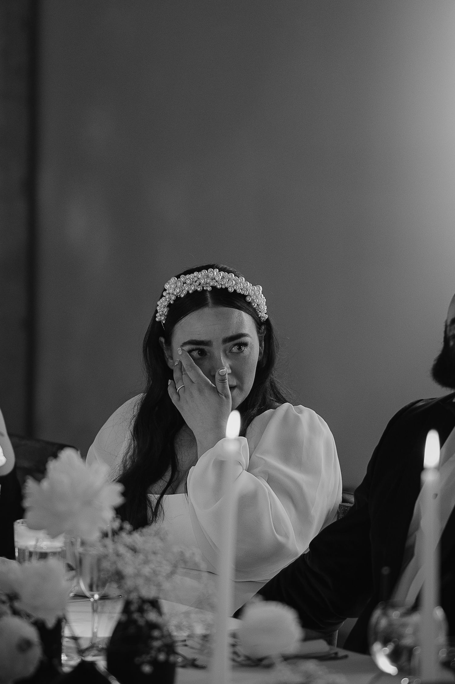 Black and white reception photo showing an emotional moment at a candlelit dining table.