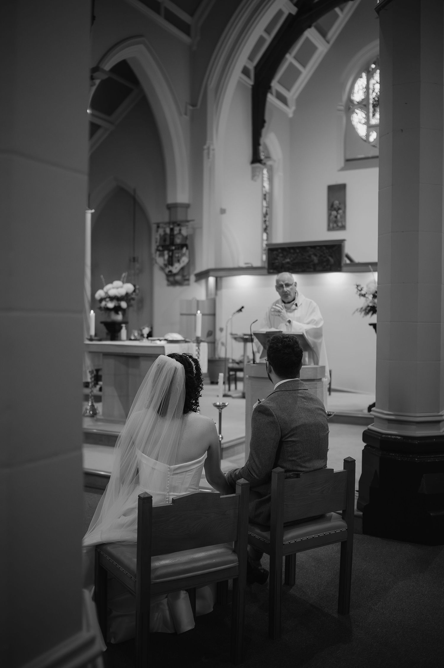 A black and white photo of a wedding ceremony in a church with arched architecture.