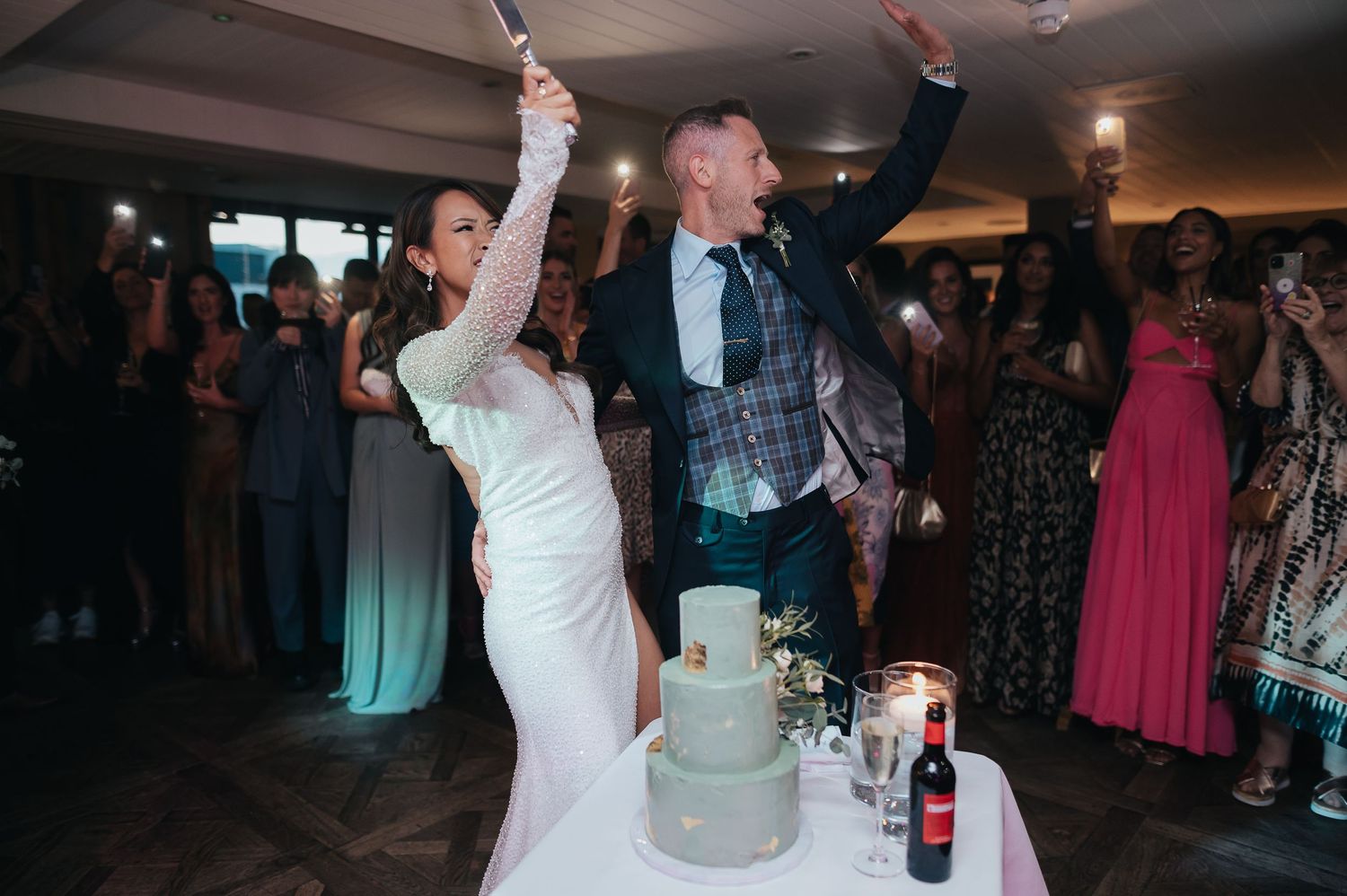 Newlyweds celebrating beside their modern three-tier wedding cake.