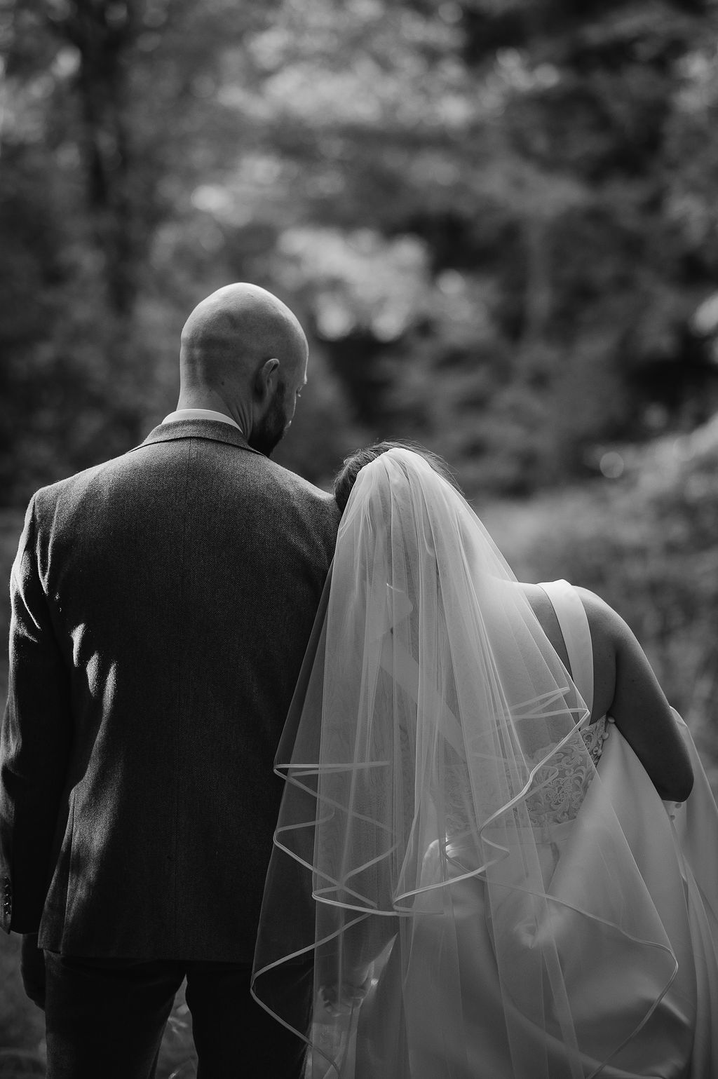 Black and white intimate portrait of newlyweds from behind in a wooded setting.
