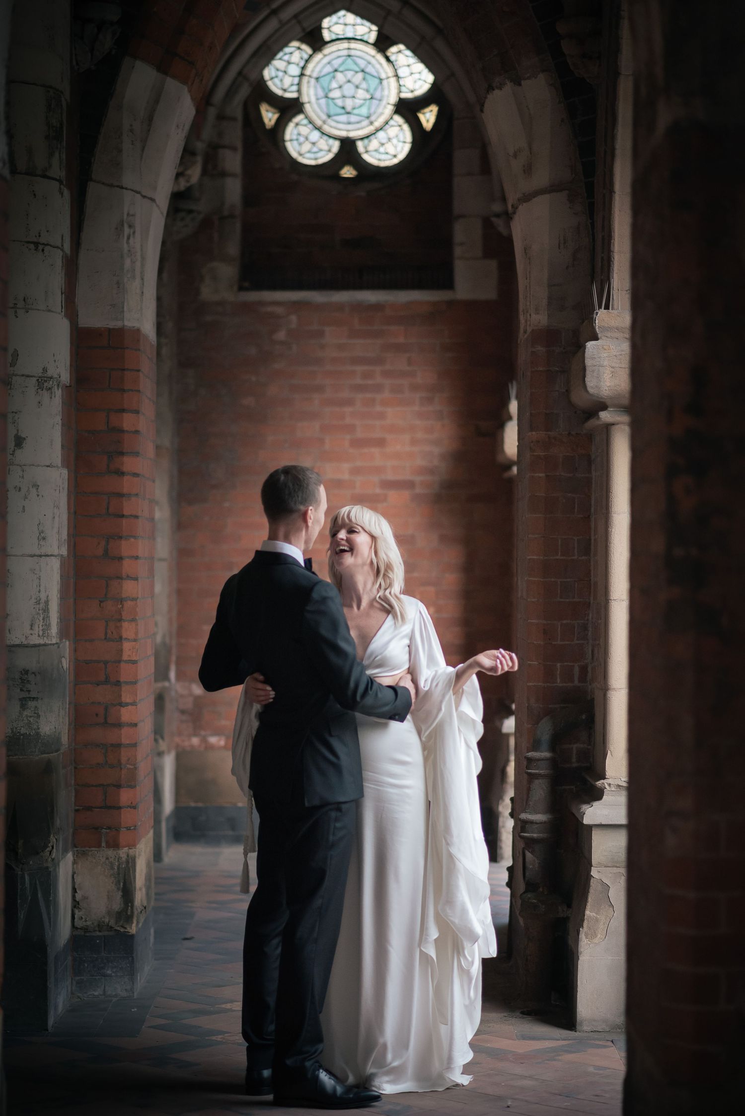 A couple shares a romantic moment in a gothic church archway beneath a stained glass window.