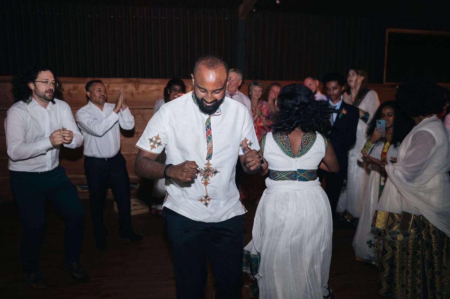 Wedding reception guests dancing together in dimly lit venue.