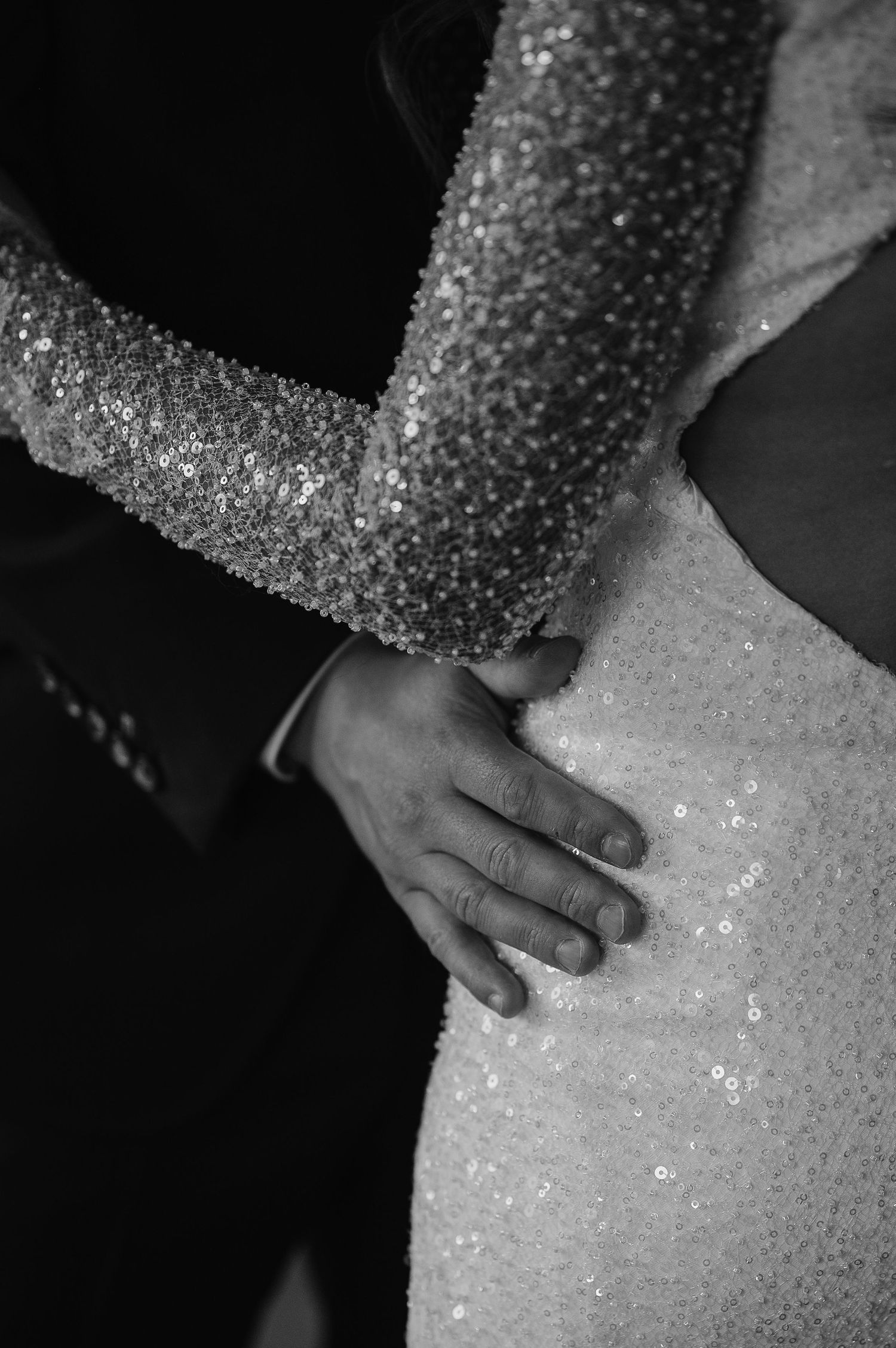 Close-up detail of a sparkling wedding dress and gentle embrace.