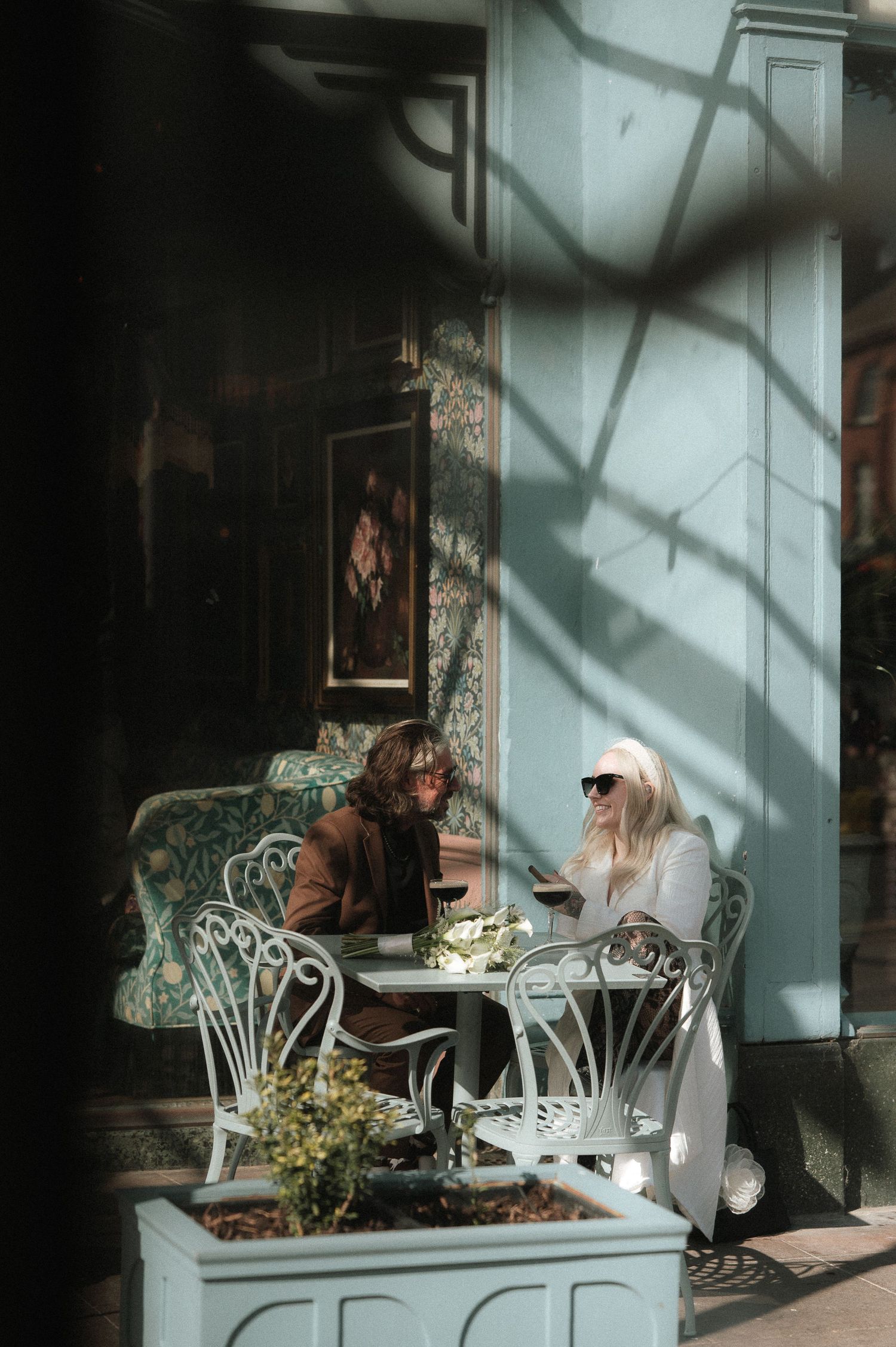 Outdoor cafe seating area with white furniture and dramatic window shadows.
