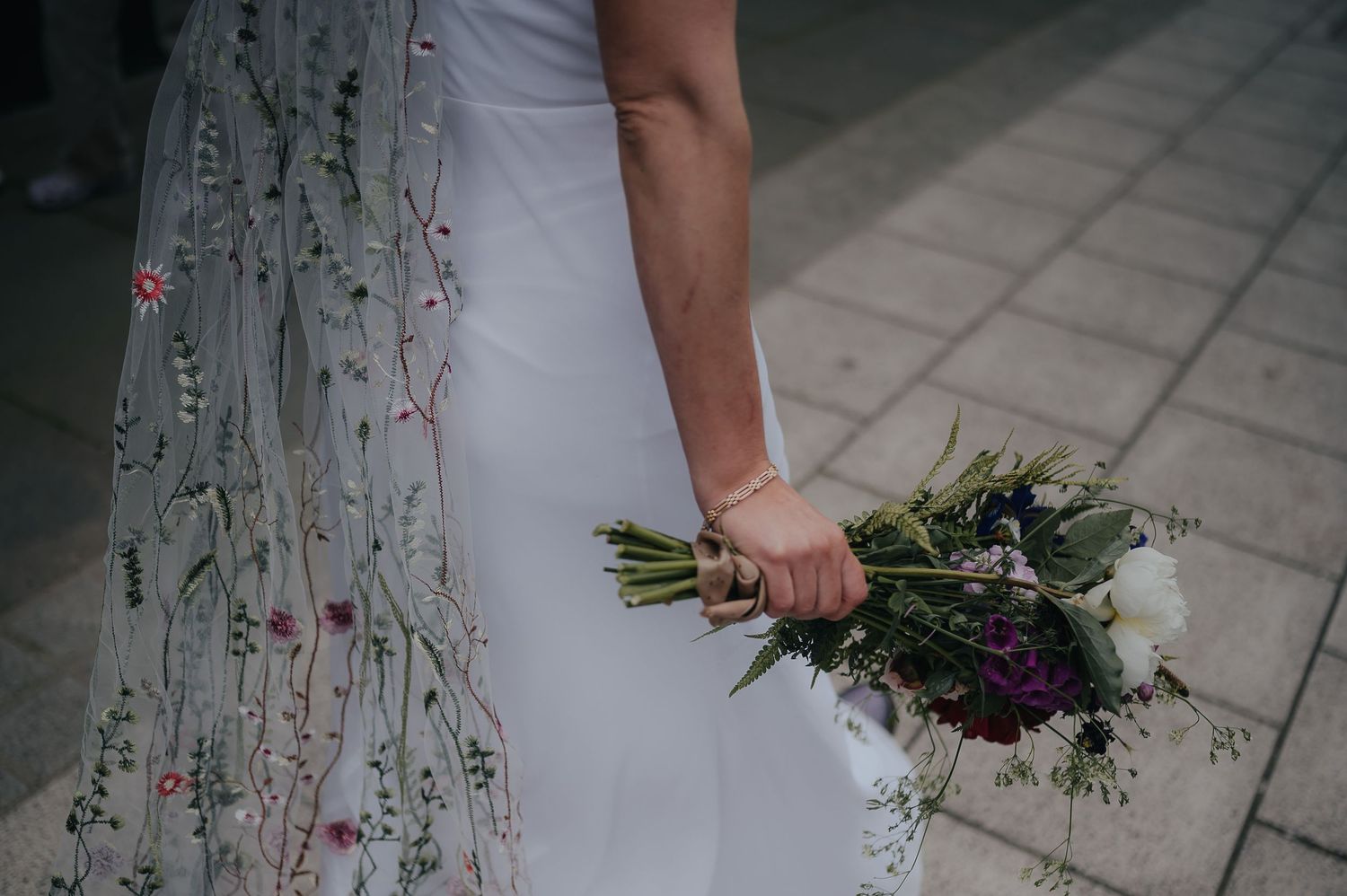 Close-up of bride holding a wildflower bouquet with delicate lace veil detail.