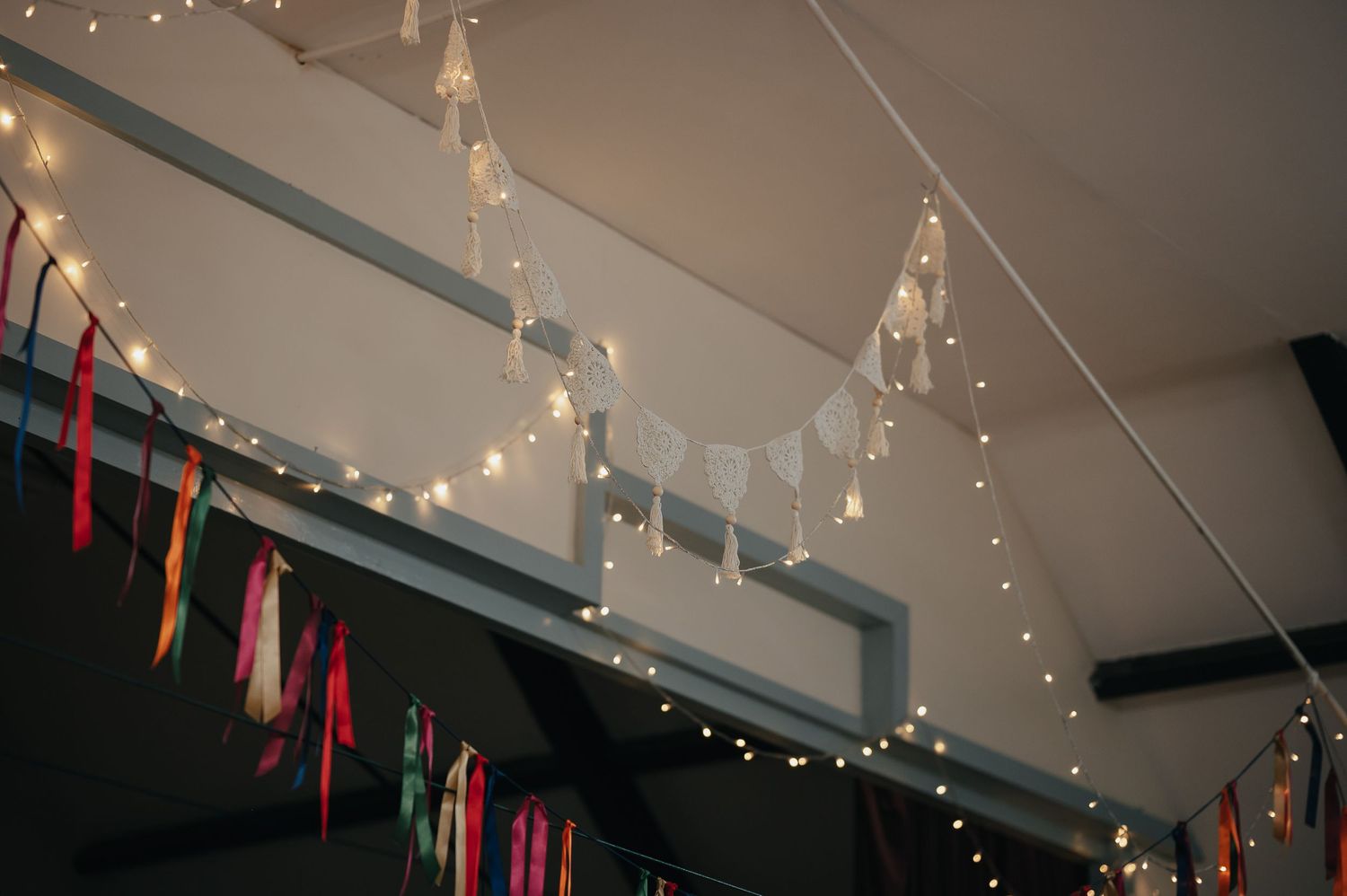 Festive string lights and colorful fabric streamers decorate wedding reception venue ceiling.