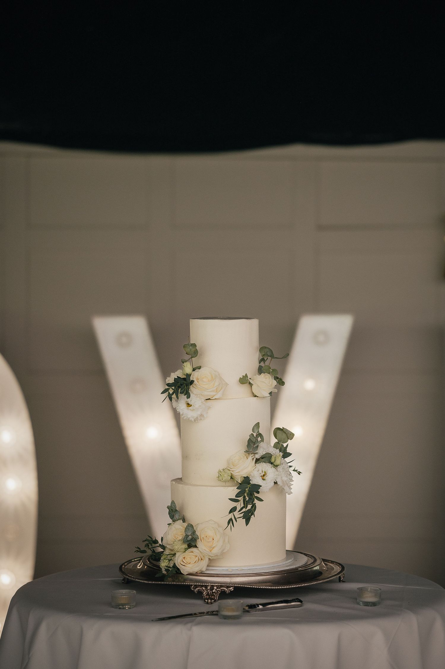 Minimalist white two-tier wedding cake decorated with fresh flowers on grey linen.