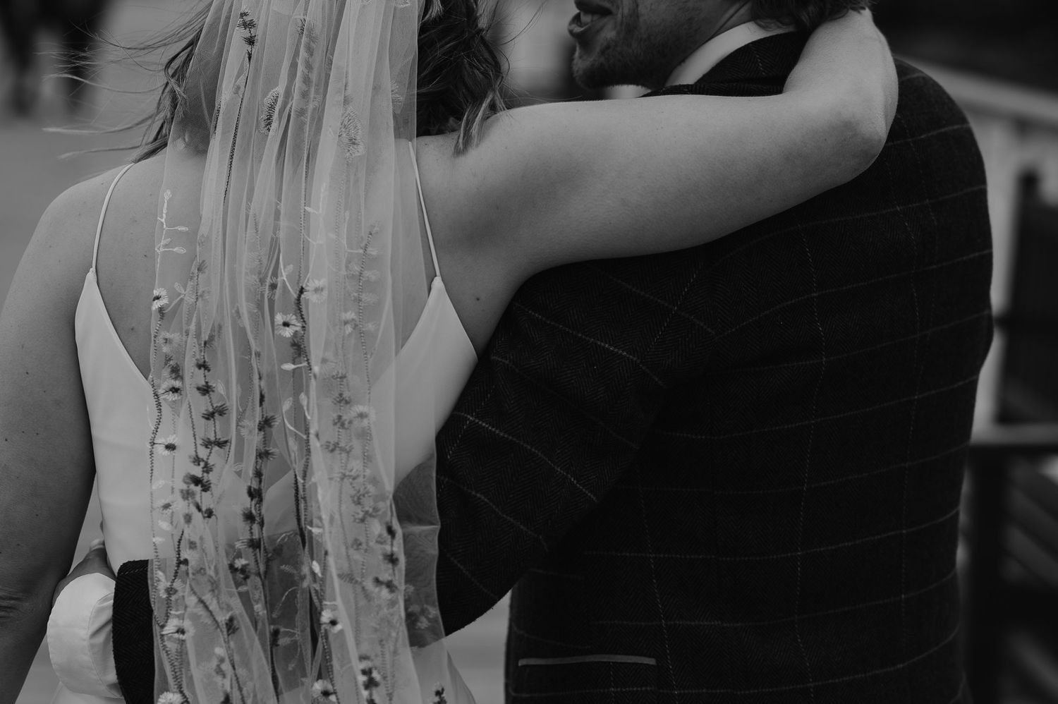 Close-up black and white detail of embroidered wedding veil and formal attire.