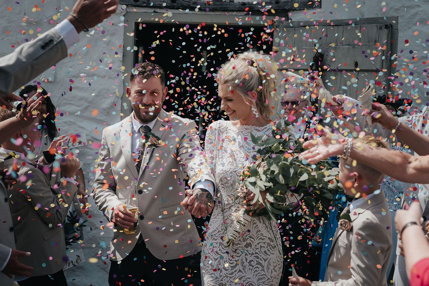 Newlyweds exit celebration with colorful confetti shower in bright daylight.