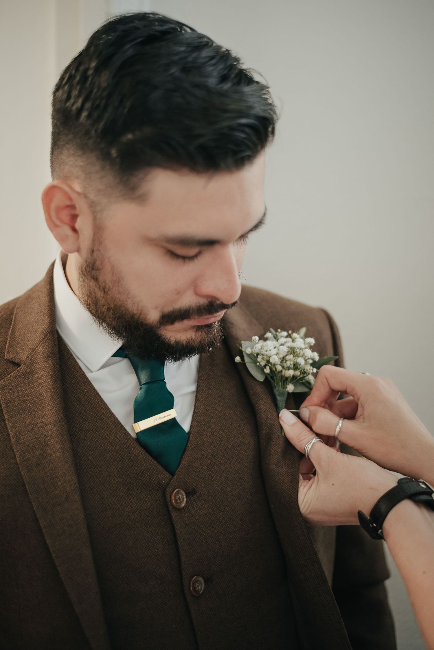 Someone pinning a white boutonniere on a brown three-piece suit.
