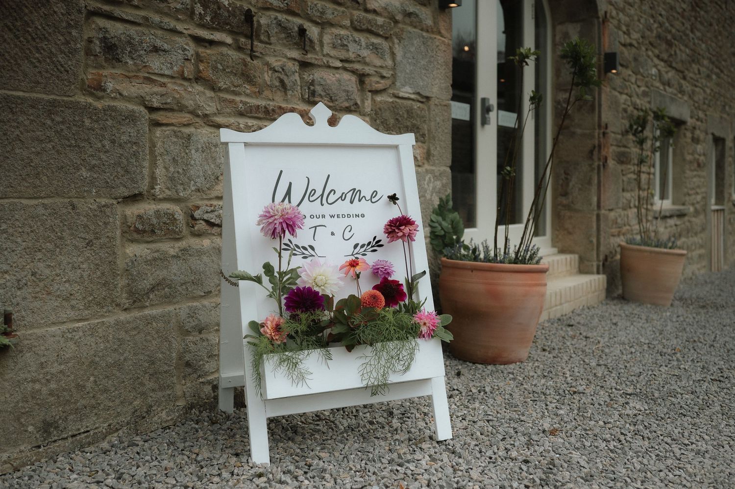 Stone wall exterior with welcome sign and potted flowers at entrance.